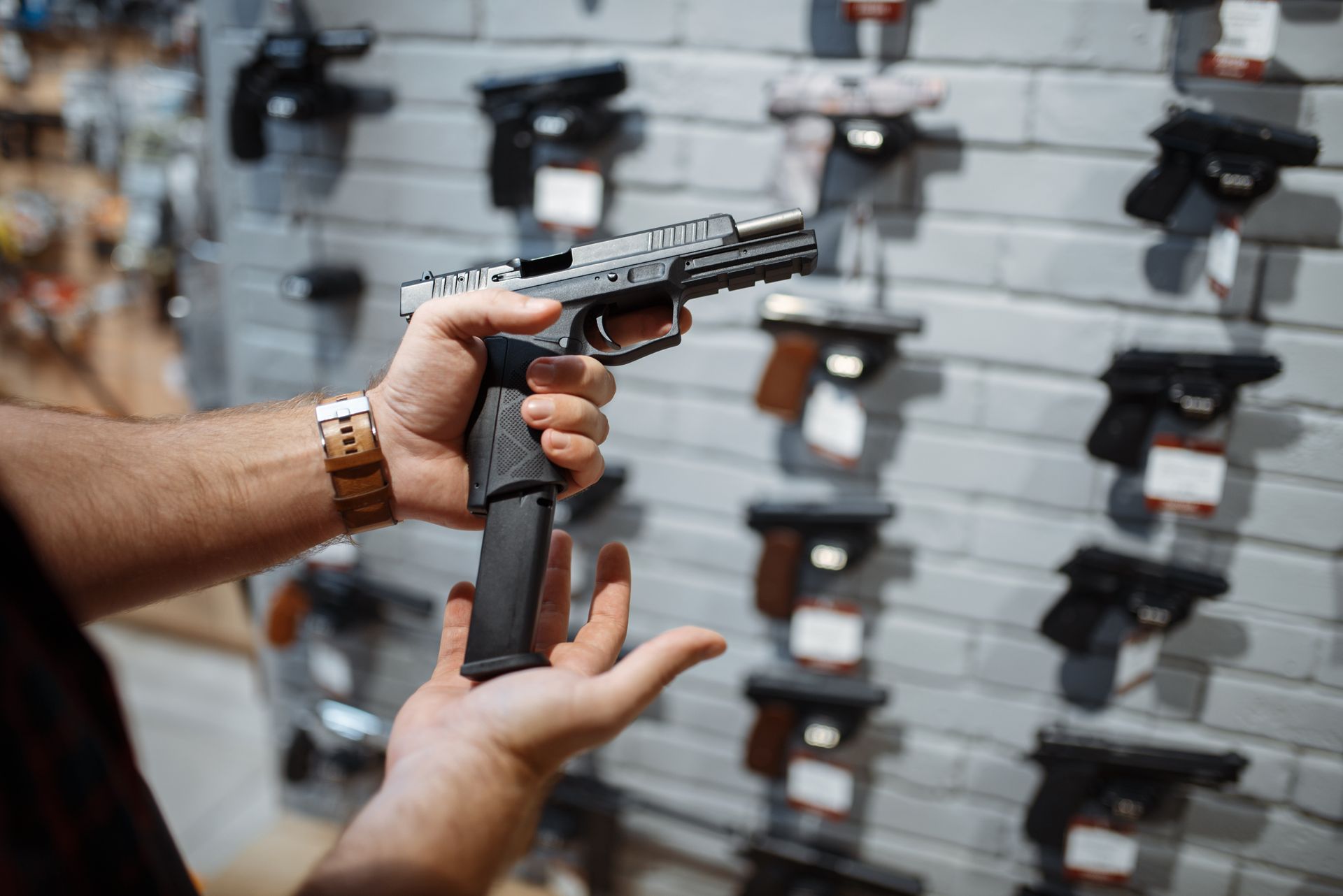Person holding a silver and black handgun in a gun store, with other handguns displayed in the background.