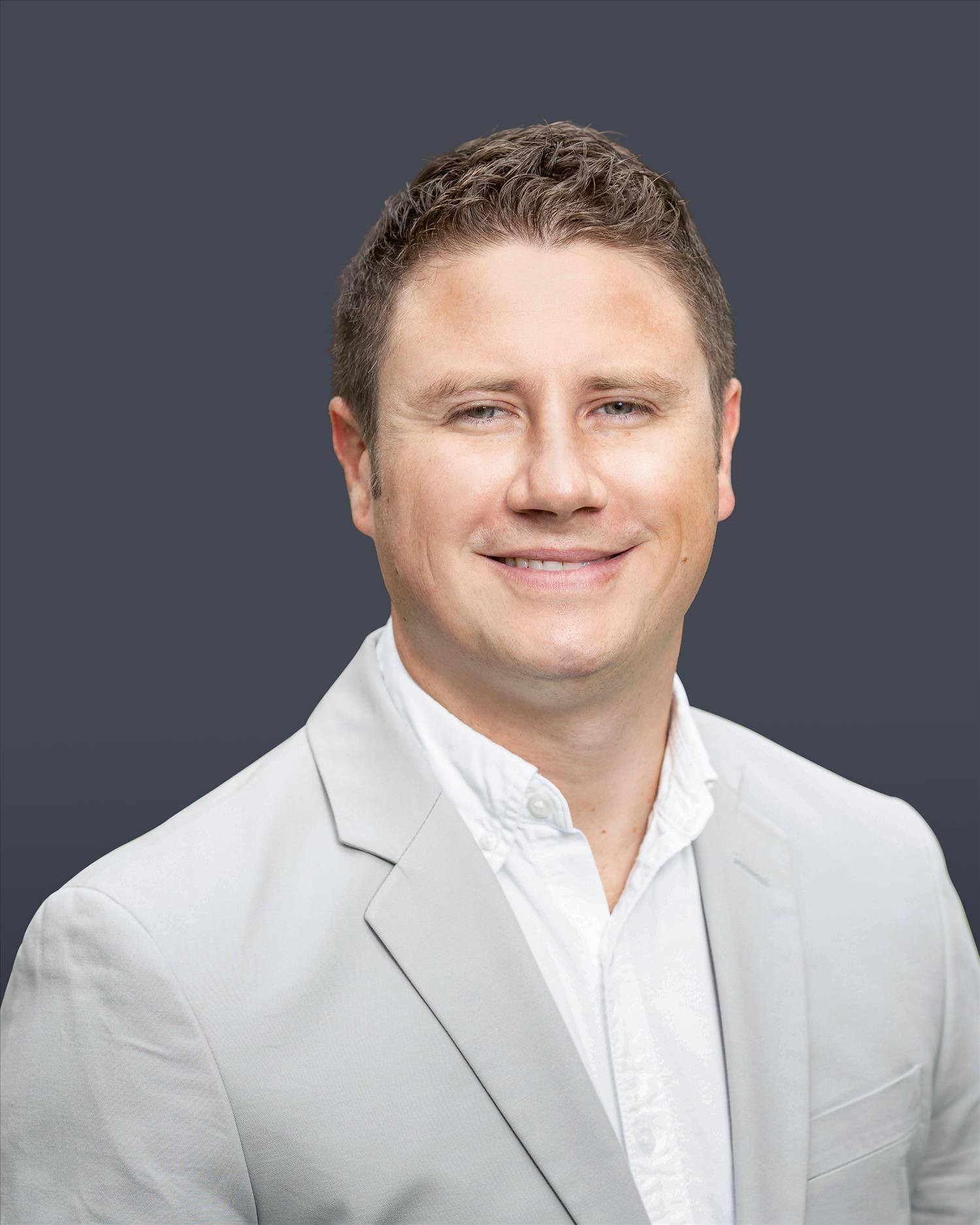 Portrait of a smiling person in a light suit against a dark gray background