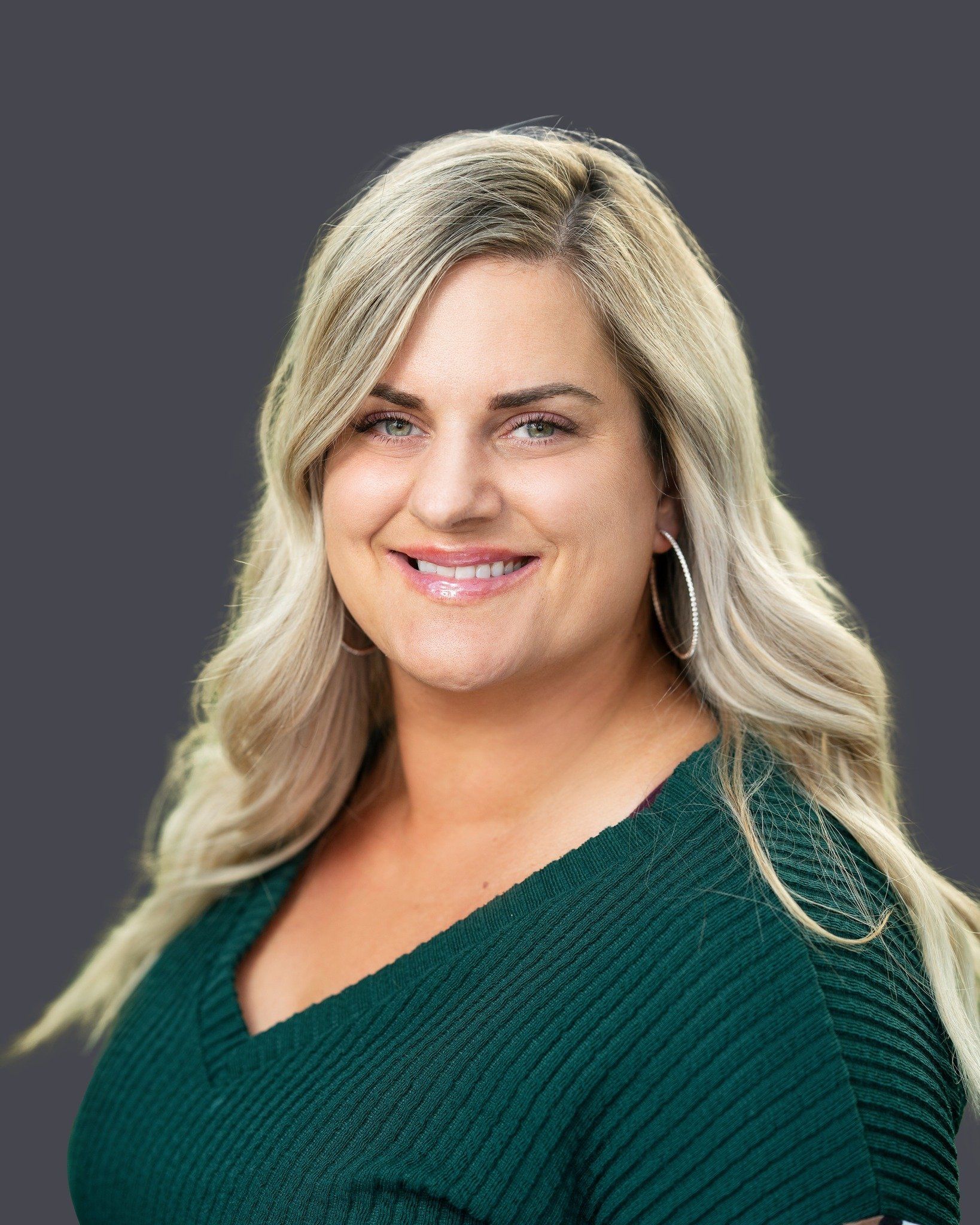 Smiling blonde woman in a dark green top against a gray background