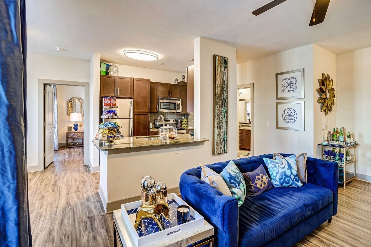 Open-concept living area with a blue sofa, kitchen island, and warm wood flooring.