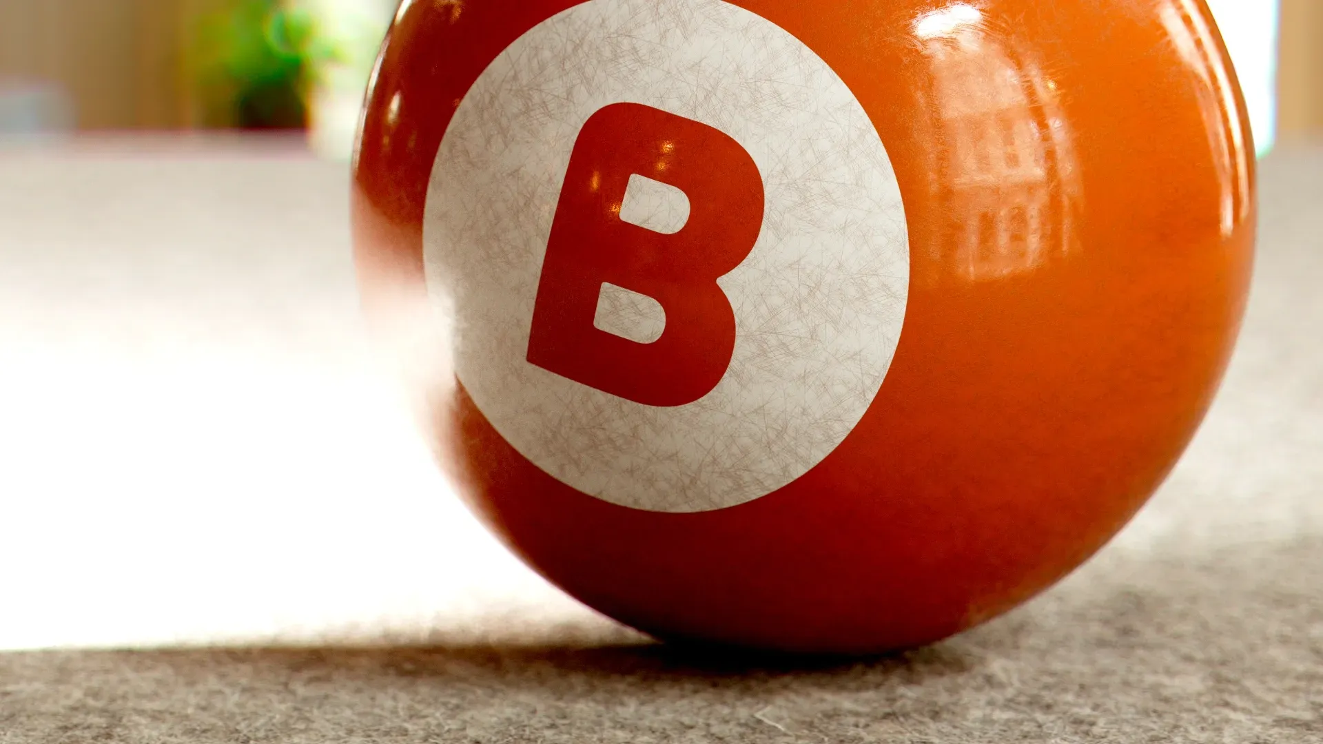 Orange lottery-style ball with a white circle and red letter B on a tabletop