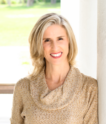 Woman with blonde hair smiling, wearing a textured beige top, against a gray backdrop.