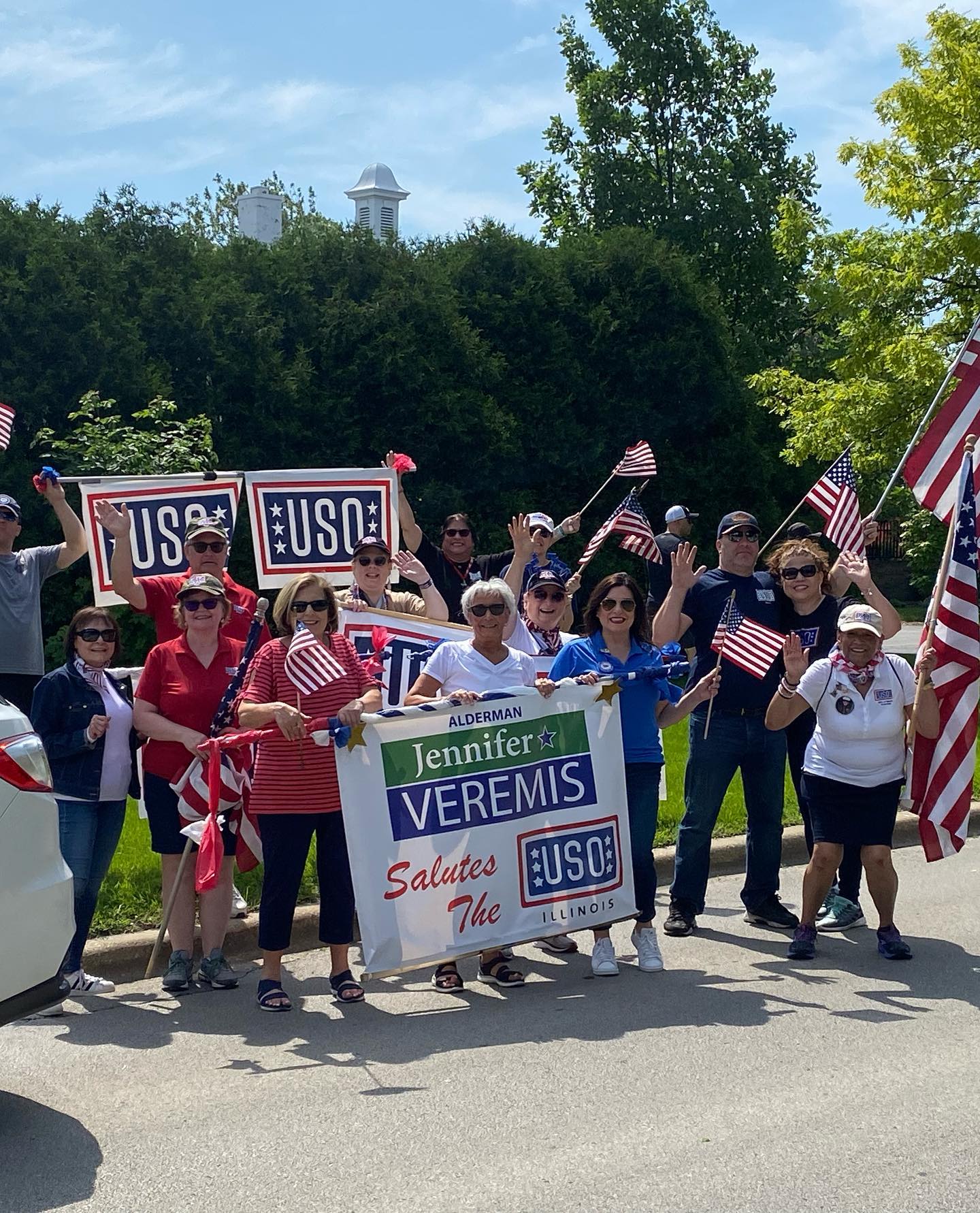 A group of people are standing on the side of the road holding flags and signs.