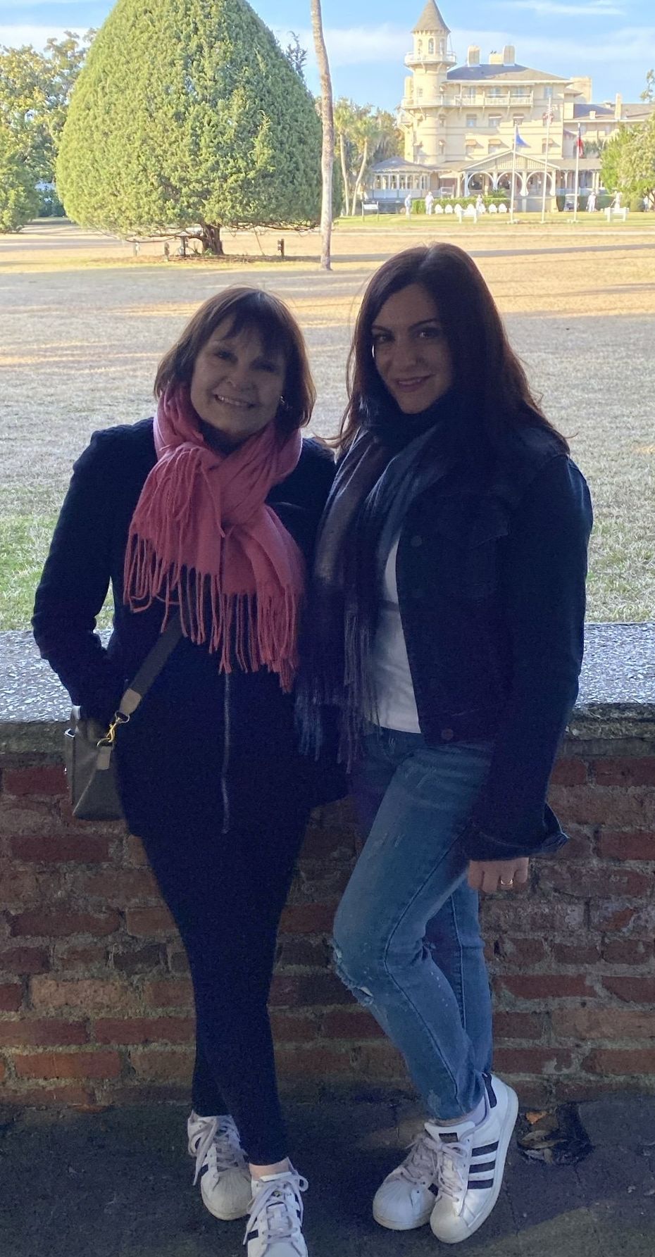 Two women are standing next to each other in front of a brick wall.