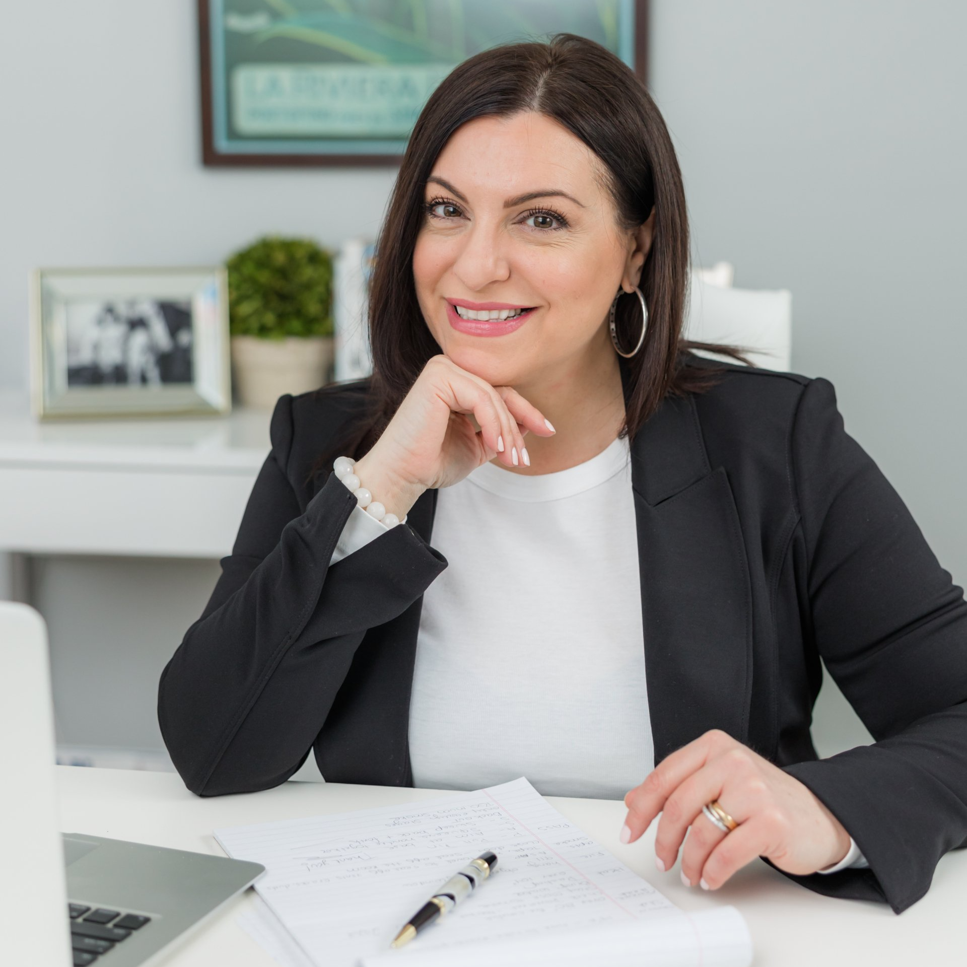 A woman in a black jacket is sitting at a desk with a laptop