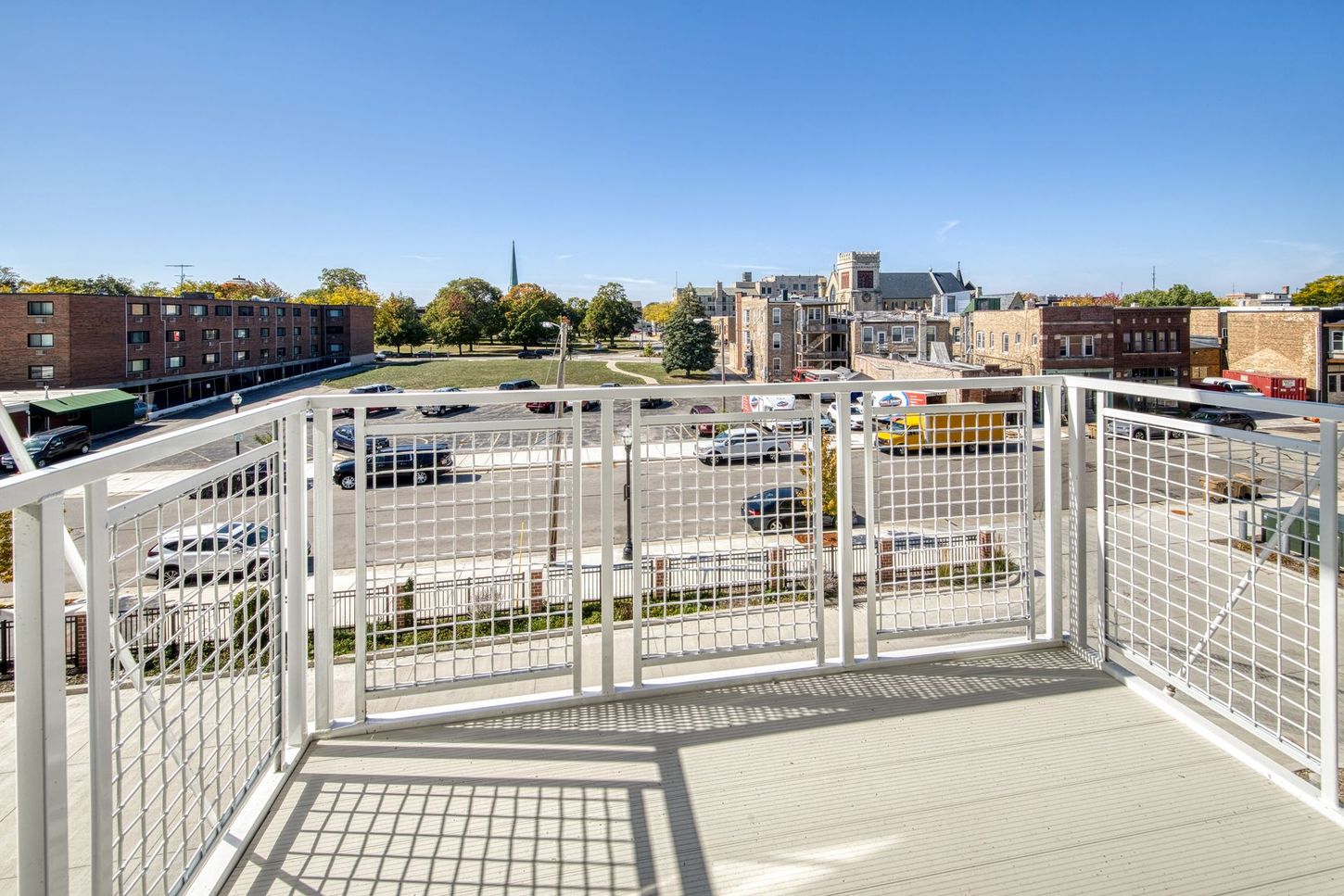 View from a white railing balcony of a city street and buildings on a sunny day.