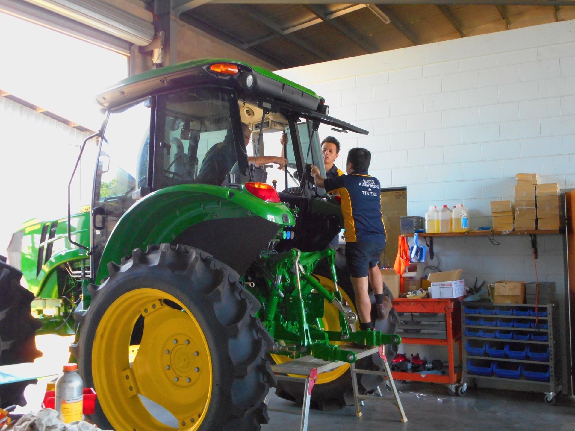 Two People Working on a Green and Yellow John Deere Tractor — Mobile Windscreens FNQ in Cardwell, QLD