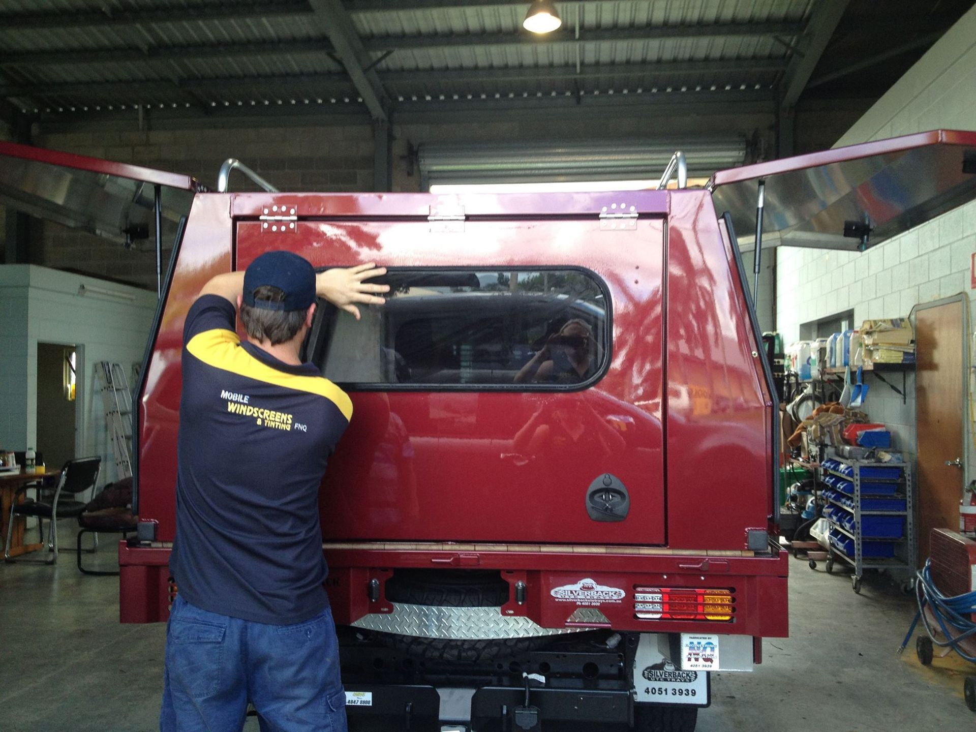 Man Installing Window on Red Truck Bed in Workshop — Mobile Windscreens FNQ in Innisfail, QLD