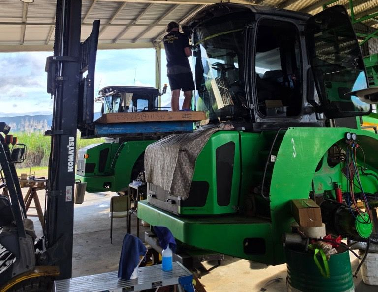 Green combine harvester under a shed, with a person working on it.