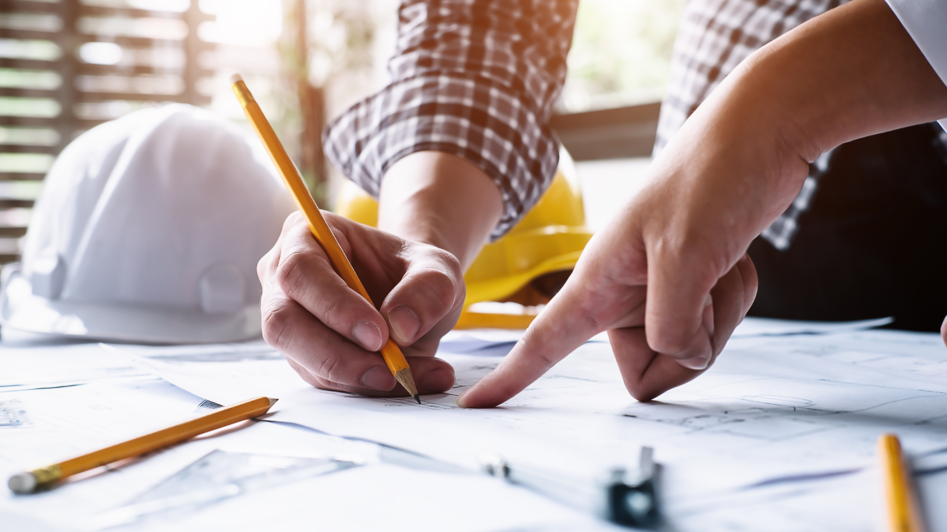 Hands sketching a blueprint with pencils on a desk, focused on design work
