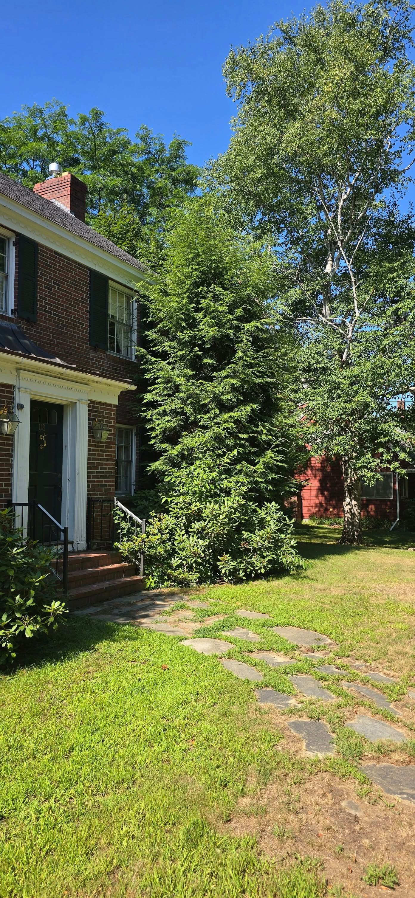 Brick house with green lawn and stepping stones. Blue sky and trees surround the house.
