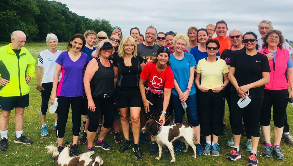 Group of people standing outdoors, many in athletic wear. Some are smiling, and a couple of dogs are present.