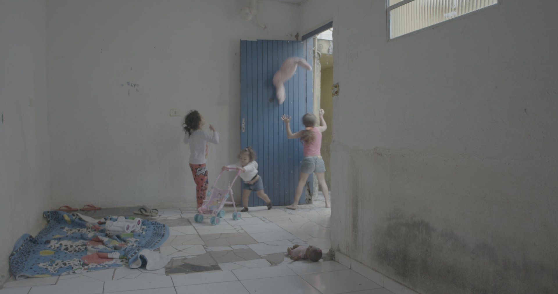 Um grupo de crianças brinca em uma sala com porta azul.