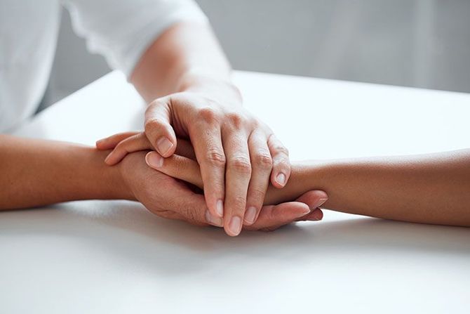 Two hands gently clasped on a white table, suggesting support or comfort