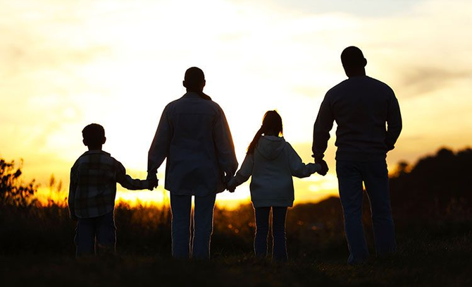 Silhouetted family of four holding hands at sunset in a field