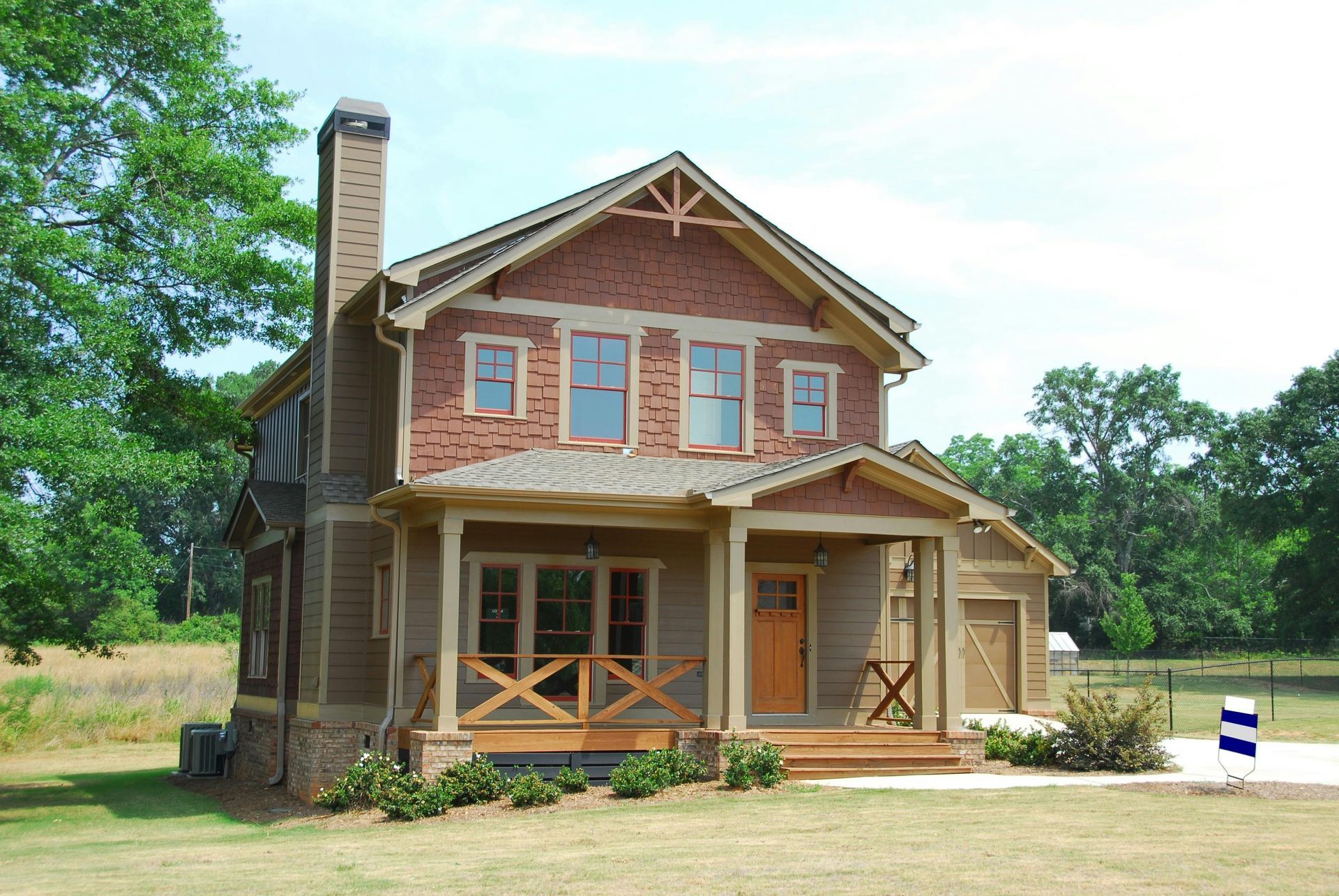 A two-story brick and siding house with a covered front porch and chimney, set in a sunny, grassy rural landscape.