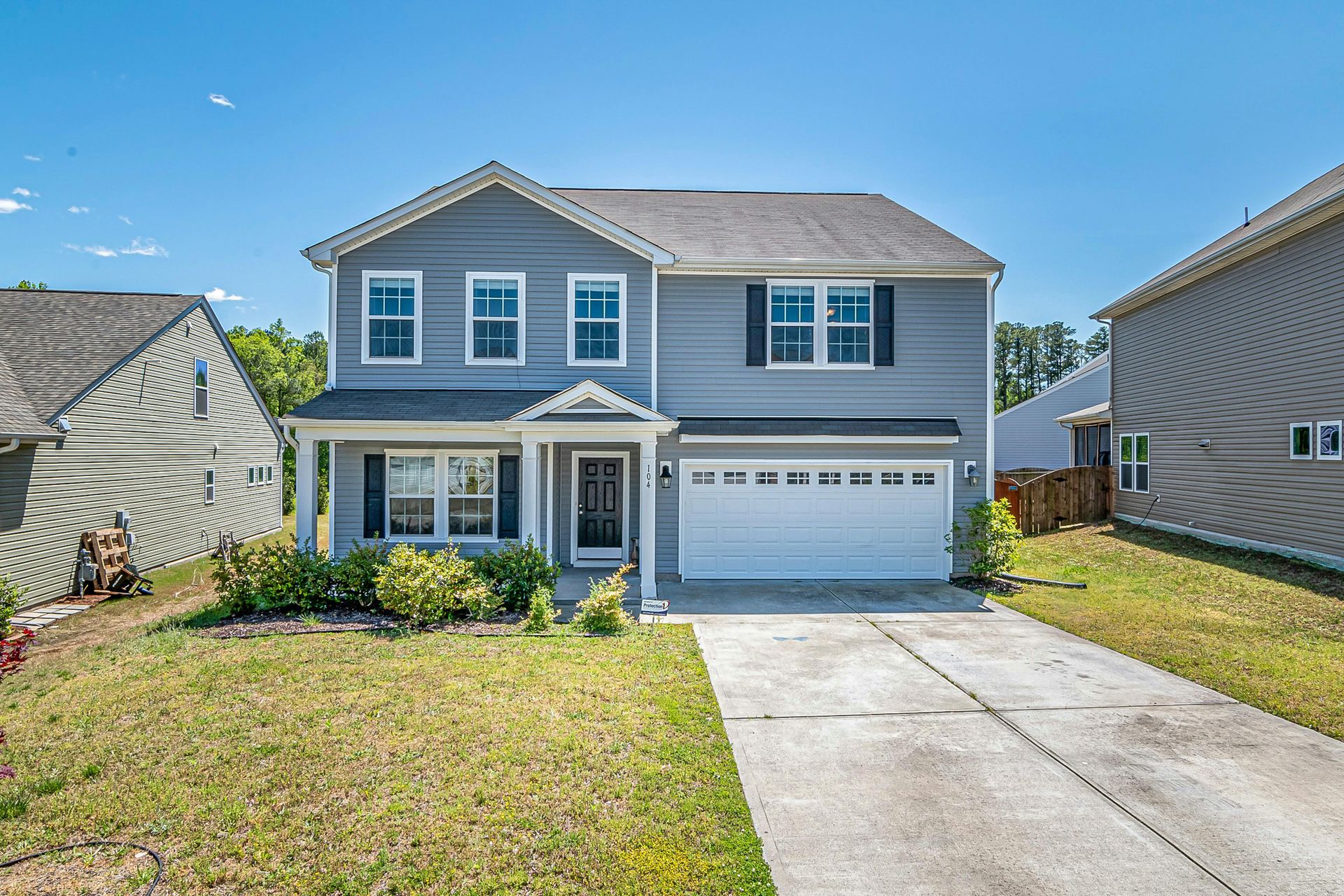 A two-story grey vinyl-sided suburban house with a white garage door, a front porch, and a concrete driveway.