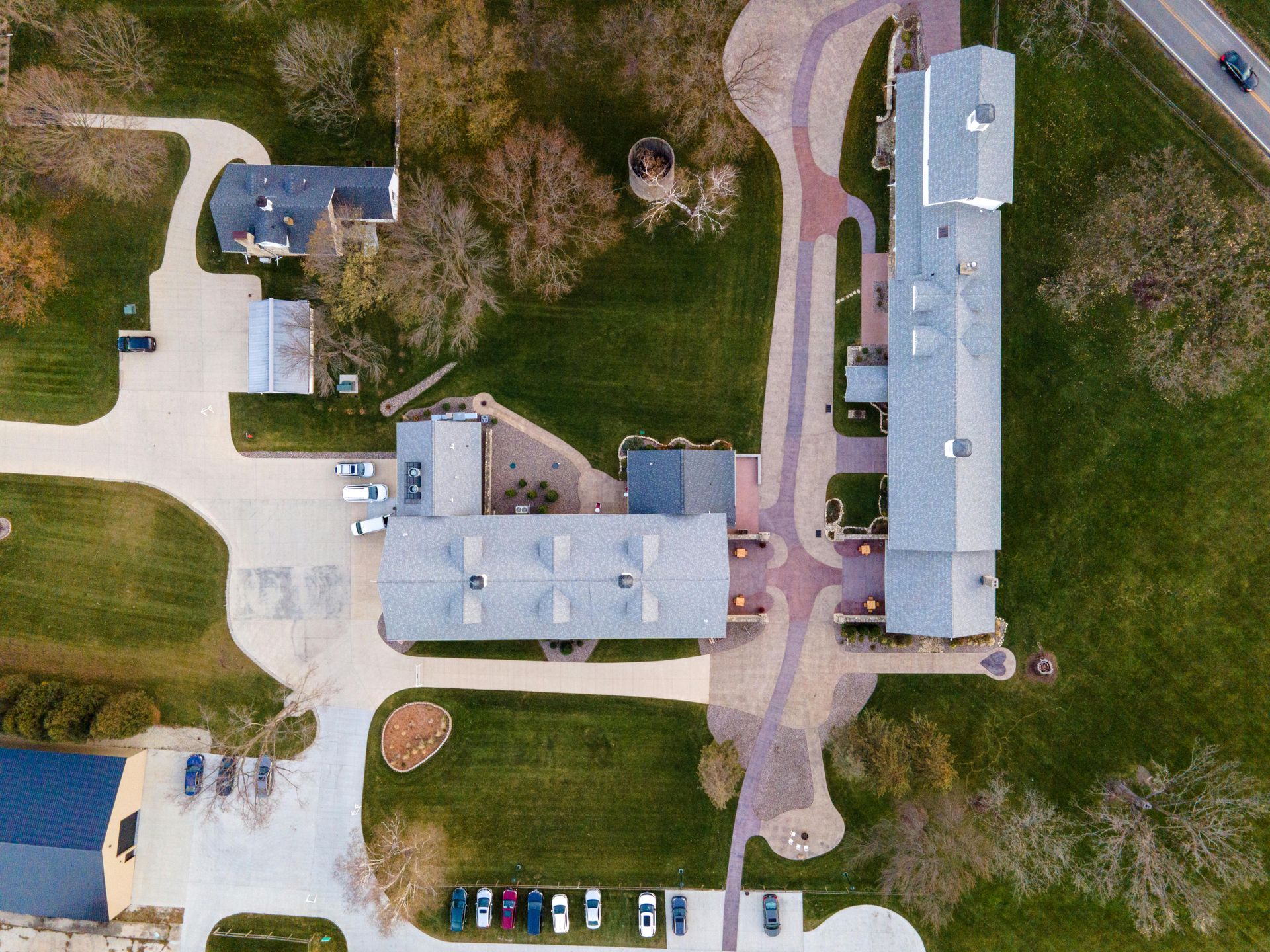 Aerial view of a sprawling complex with multiple buildings, paved pathways, and a parking lot surrounded by green lawns.