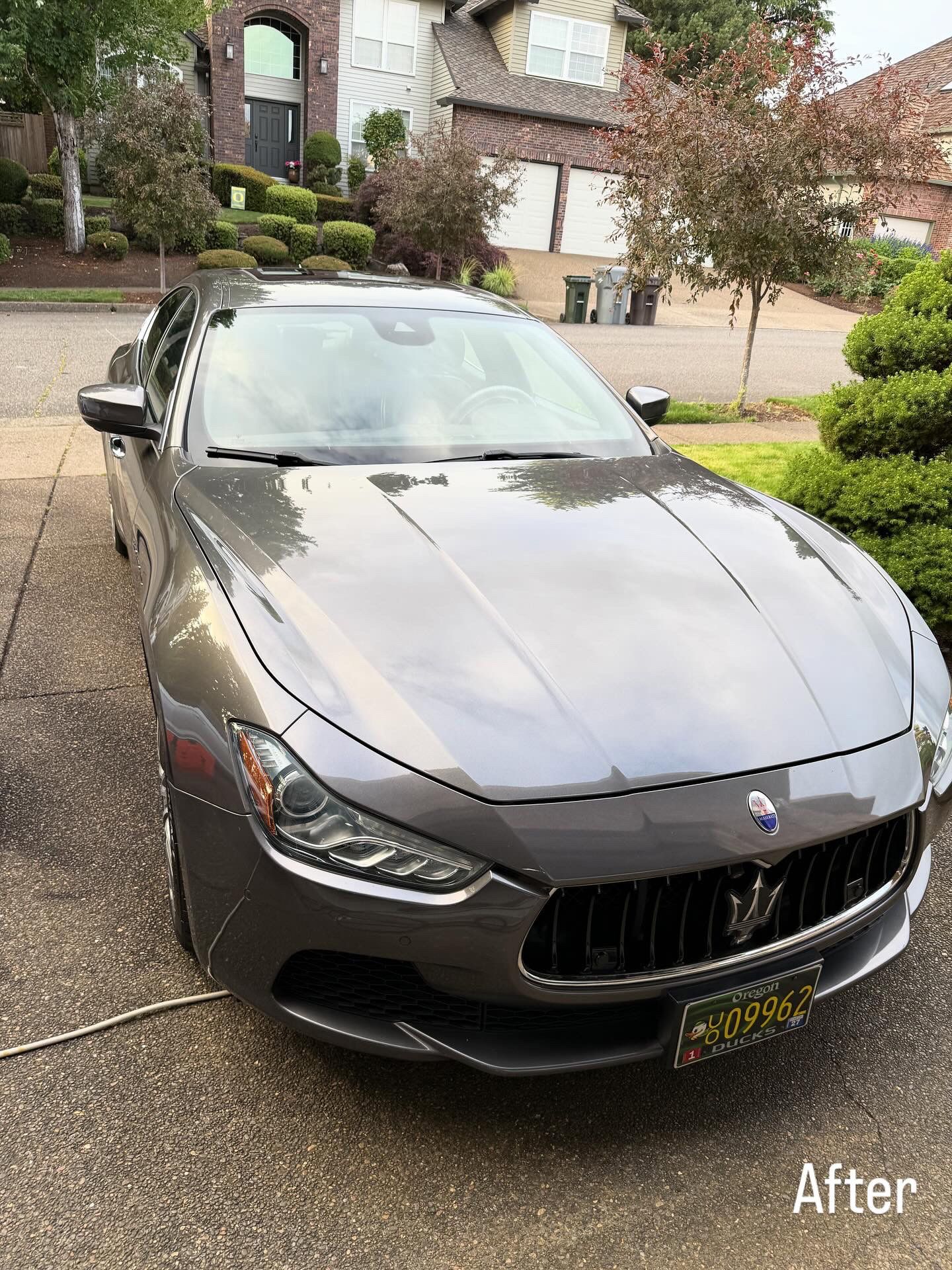 Gray Maserati sedan parked in a driveway outside a home, front view after cleaning.