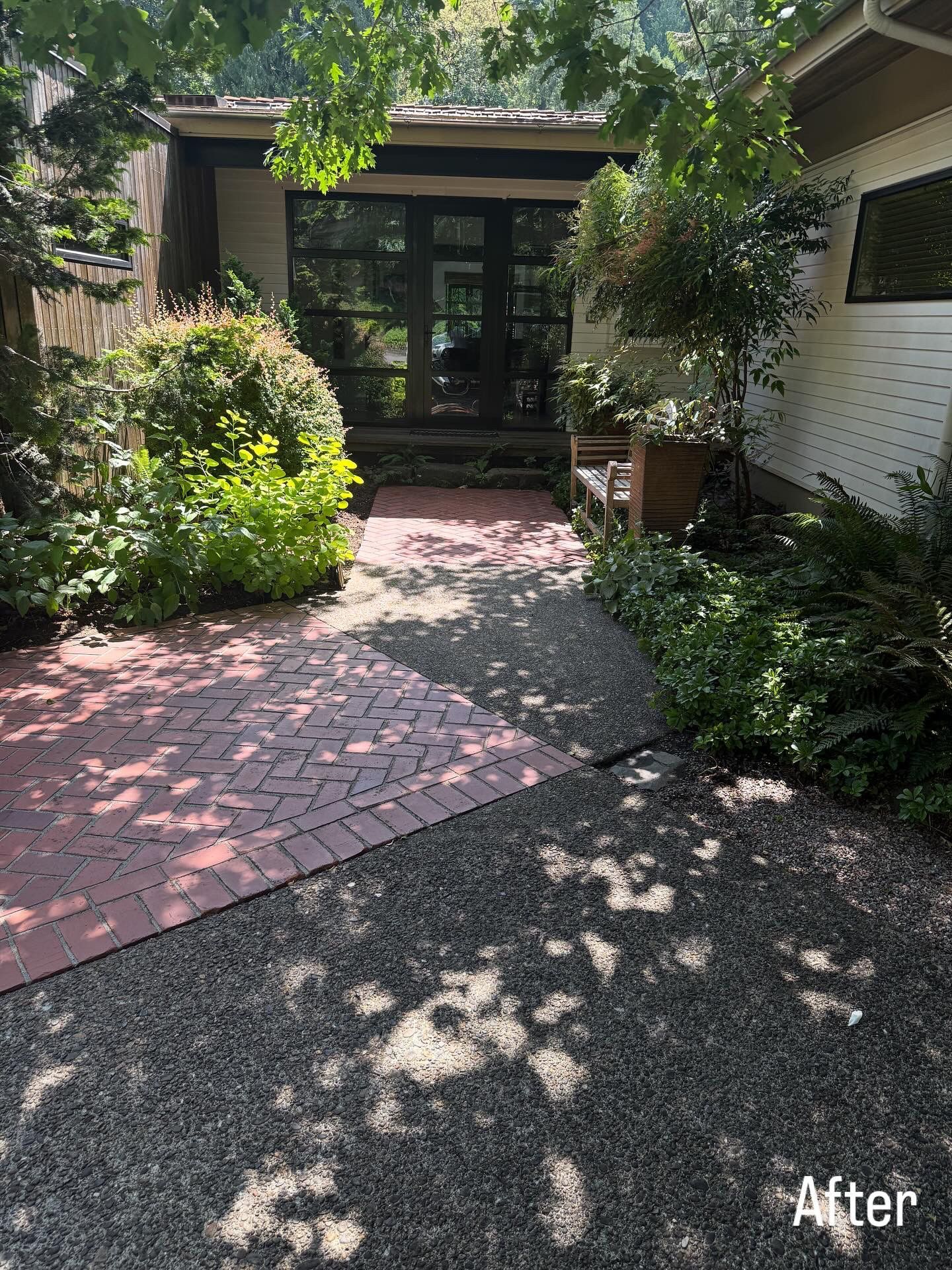Shaded front entrance with a red brick walkway, lush plants, and dark double doors.