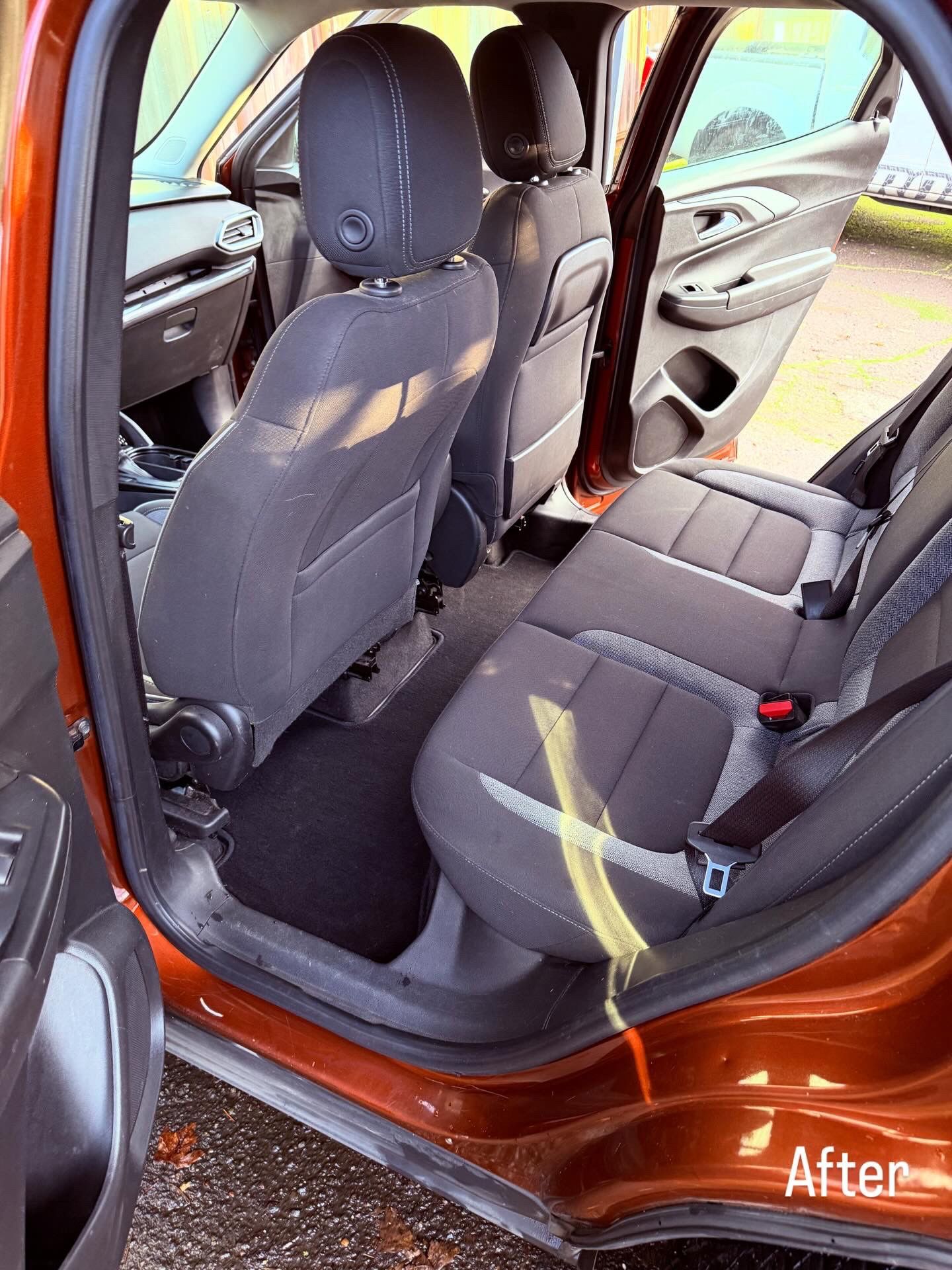 Car interior with black seats and orange exterior paint, showing the rear seat area after cleaning.