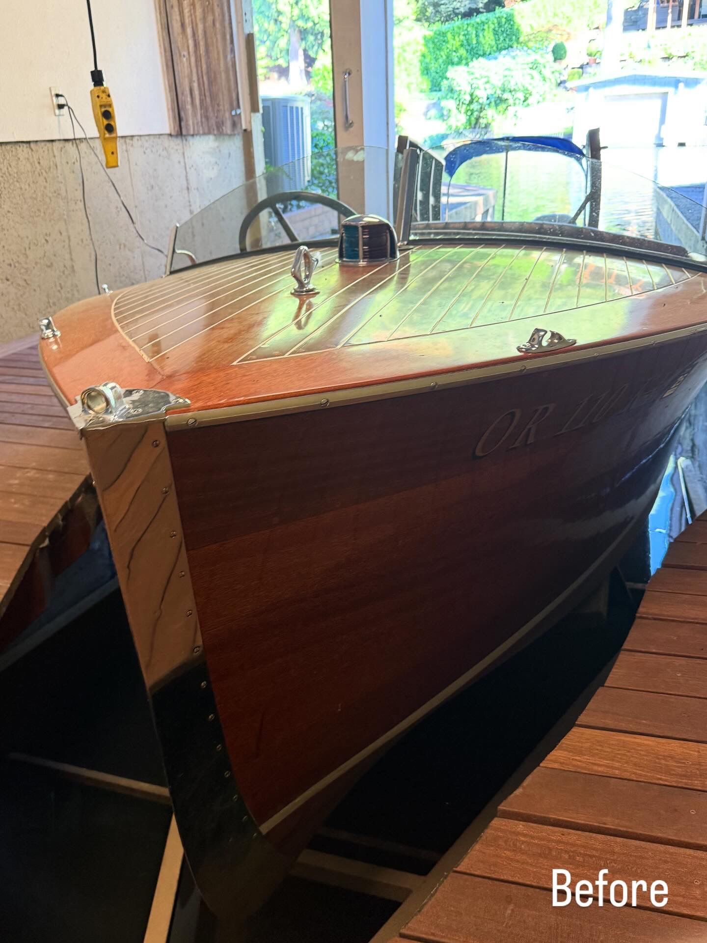 Wooden boat hull in a workshop, with a clear protective covering and “Before” label.