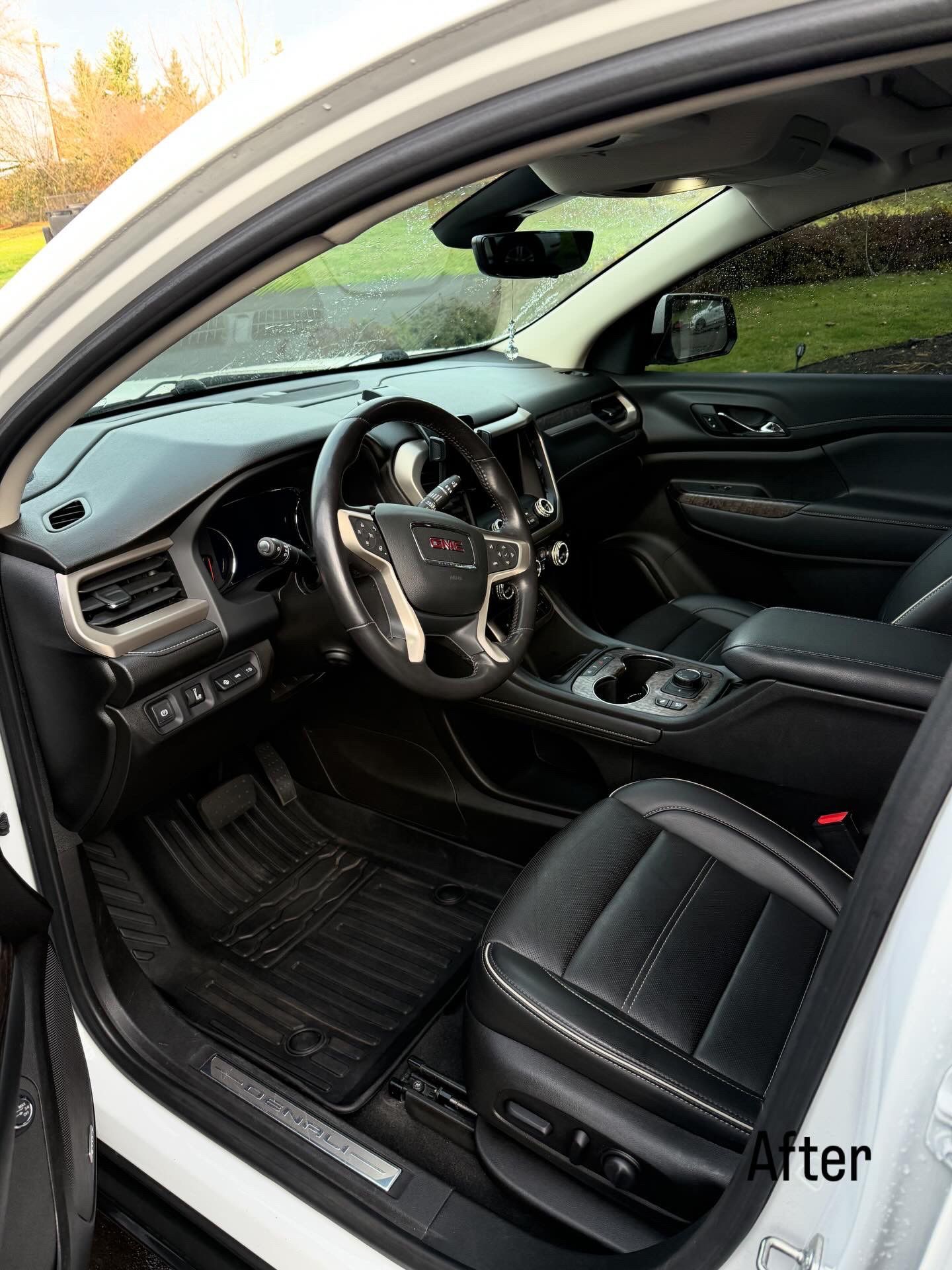 Car interior with black leather seats, steering wheel, and center console, viewed from the open driver door.