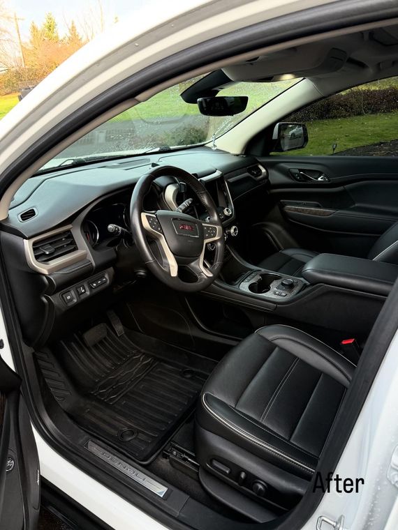 Open car door showing black leather interior, steering wheel, and dashboard with floor mats