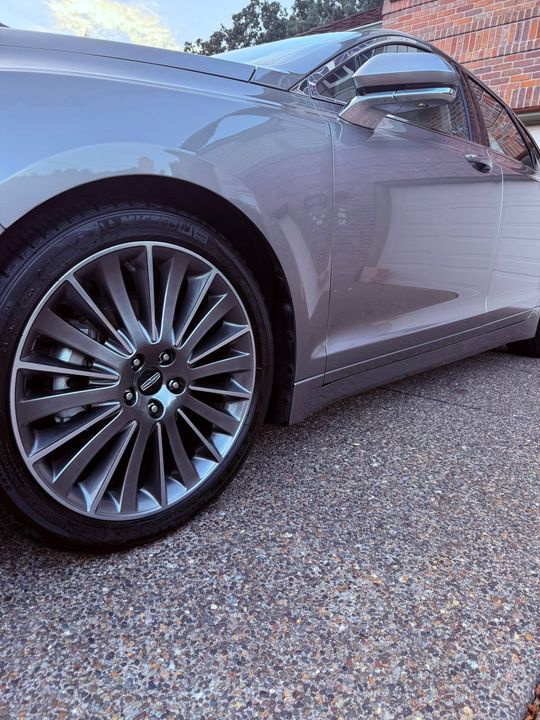 Silver BMW sports car parked on gravel, close-up of front wheel and side panel.