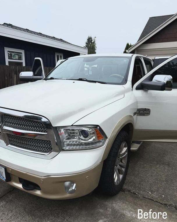 White and tan pickup truck parked in a driveway, front view with driver door open.