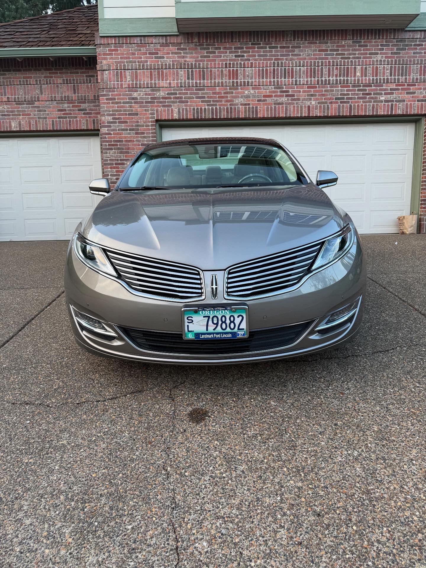 Gray sedan parked in a driveway in front of a brick garage, front view.
