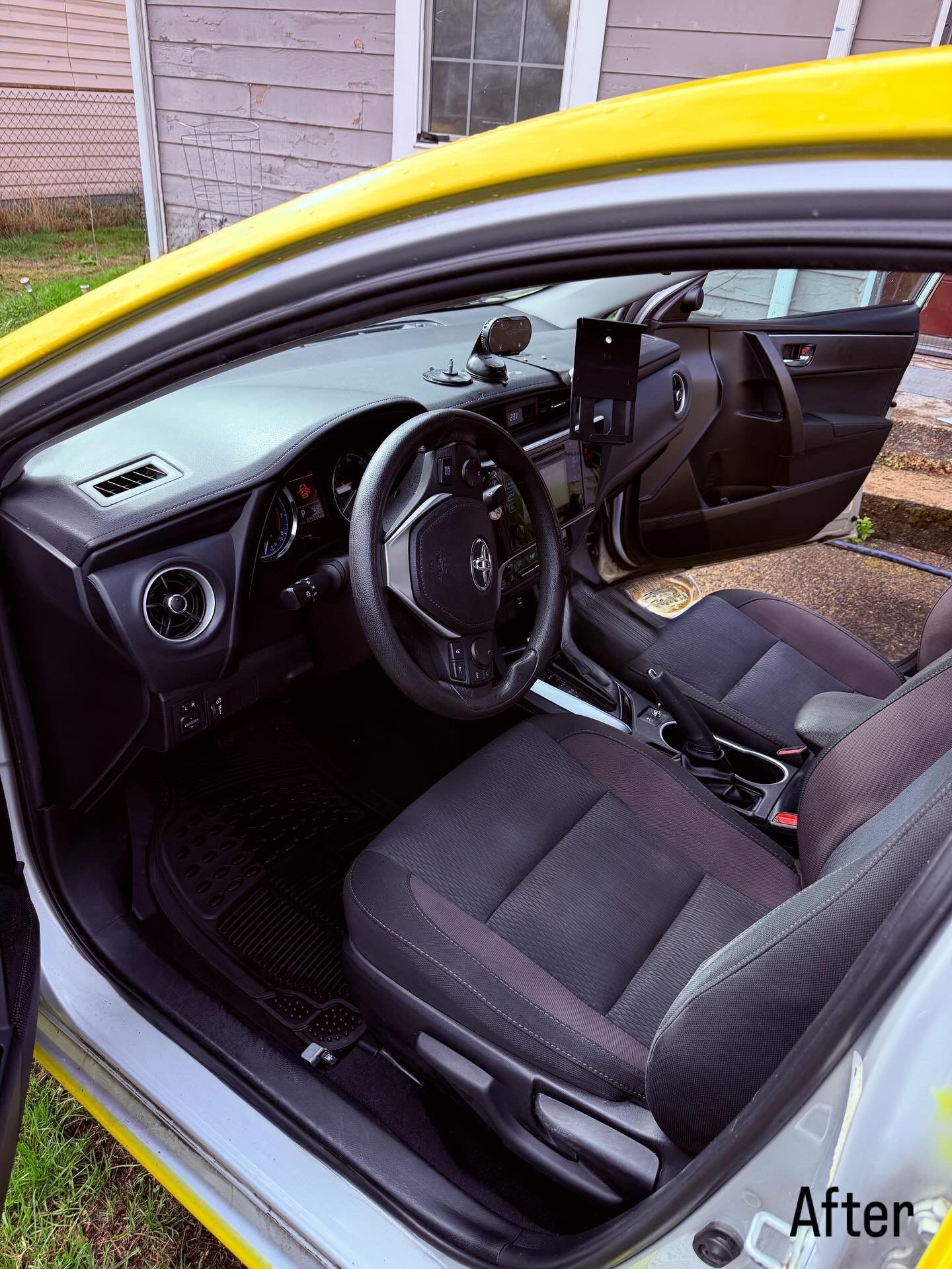 Car interior after cleaning, with black seats and open driver’s door.