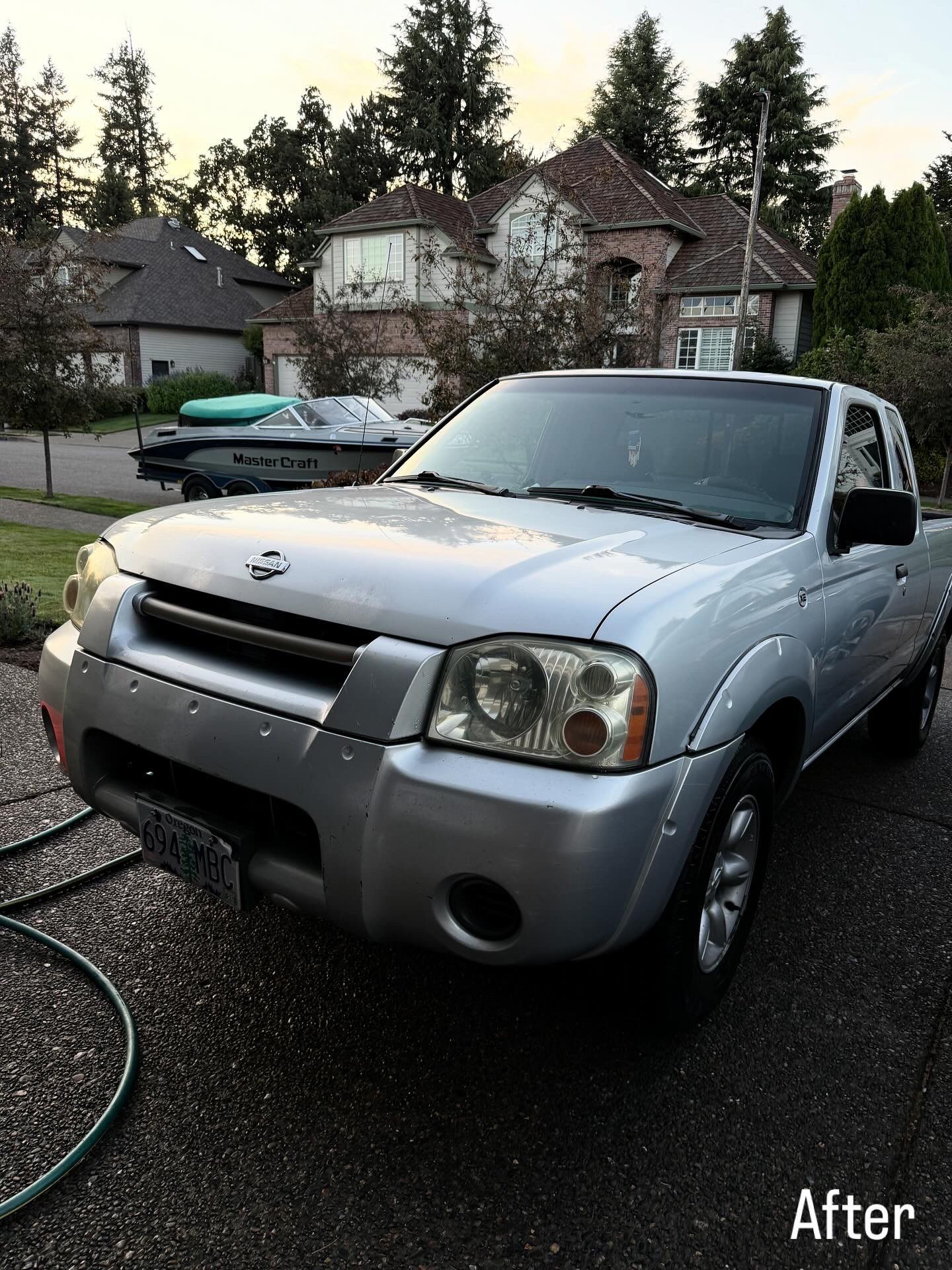 Silver pickup truck parked on a driveway at dusk, with houses and trees in the background.