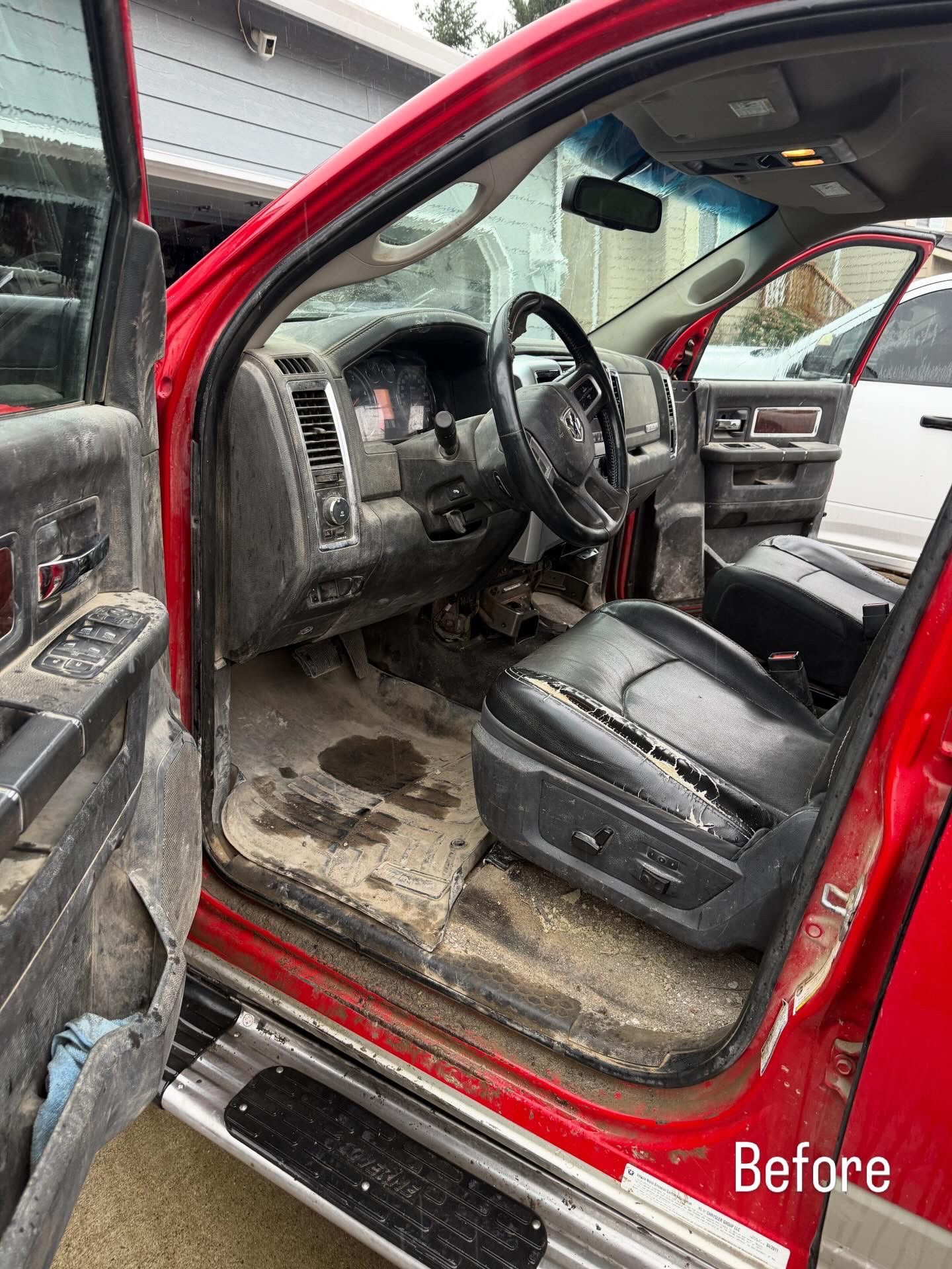 Red truck interior before detailing, with dirty black leather seat and open driver’s door.