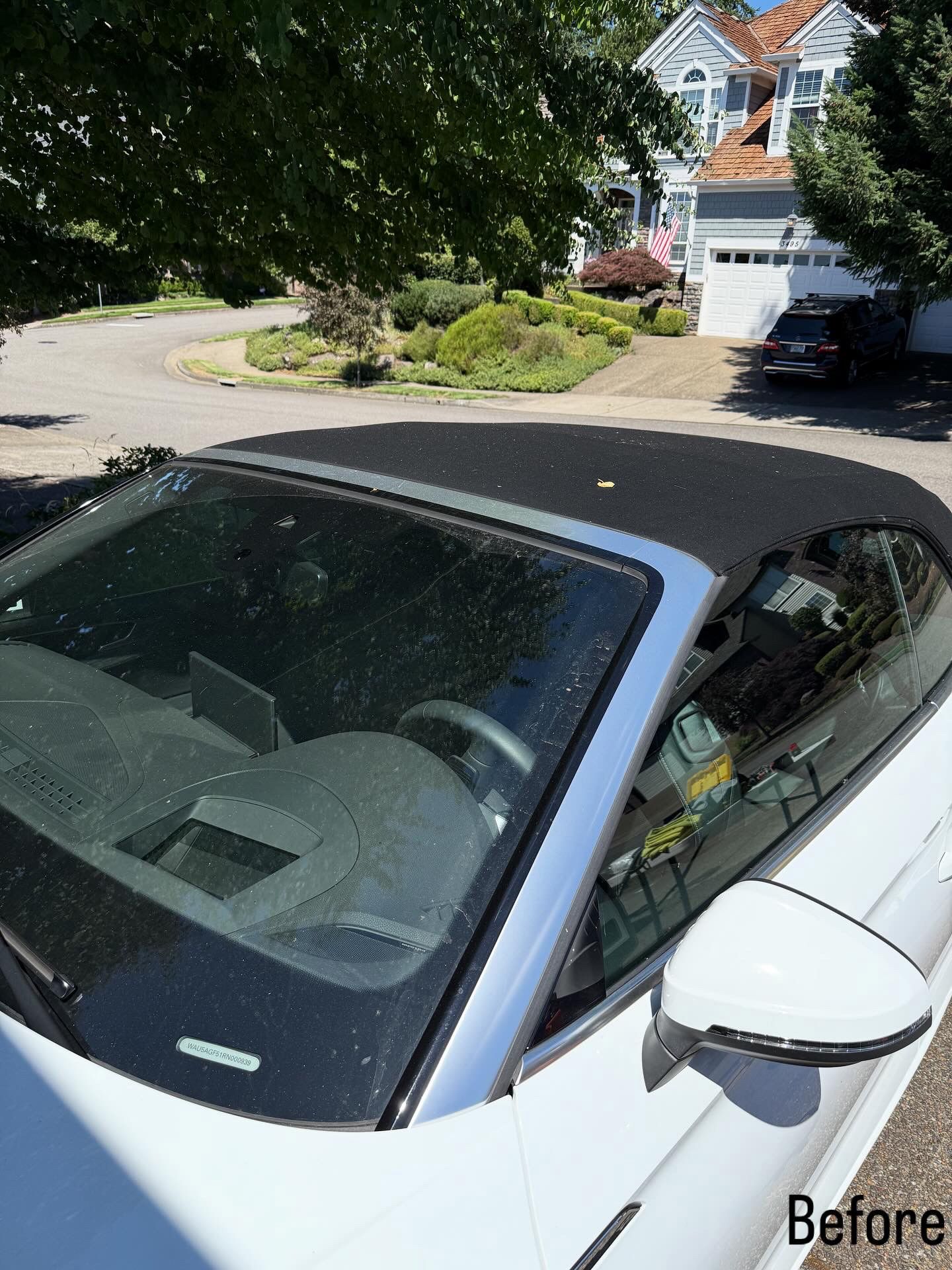 White convertible parked in a driveway beside a leafy suburban house with a garage.