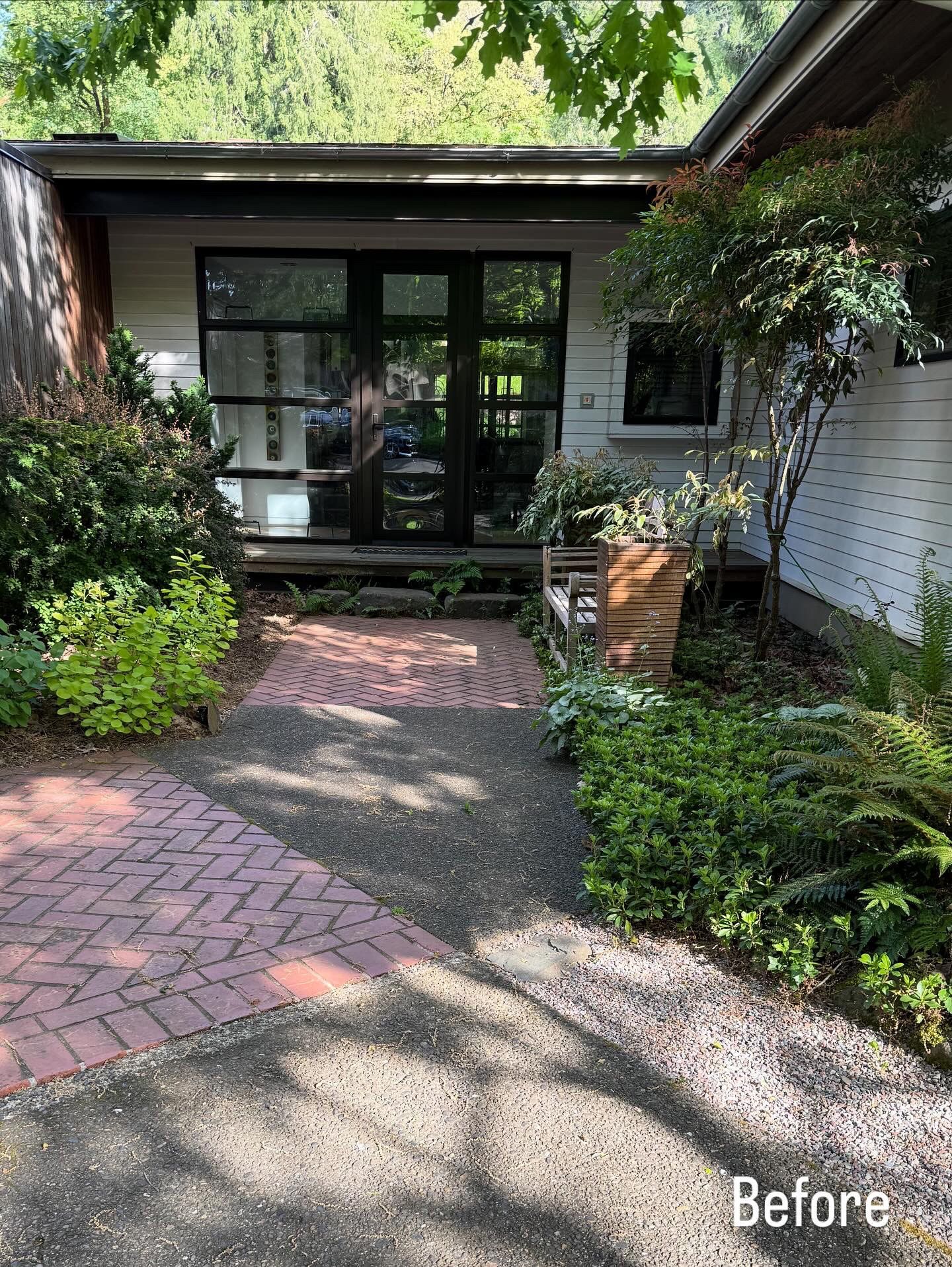 Front garden path leading to a house entrance with brick pavers, lush greenery, and white siding