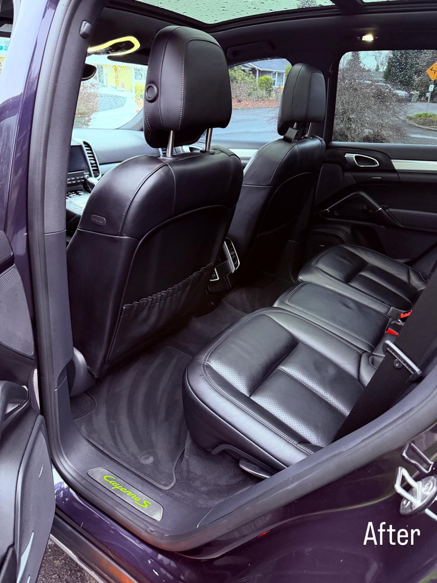Rear car seat area with black leather seats and open door, showing a clean interior after detailing.