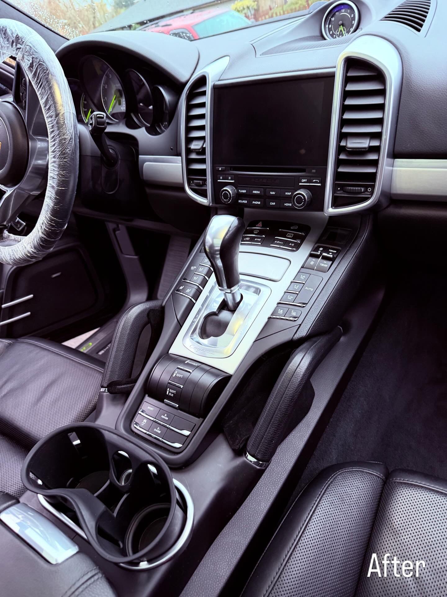 Car interior with dashboard, center console, touchscreen, gear shifter, and cupholders in a sleek dark finish