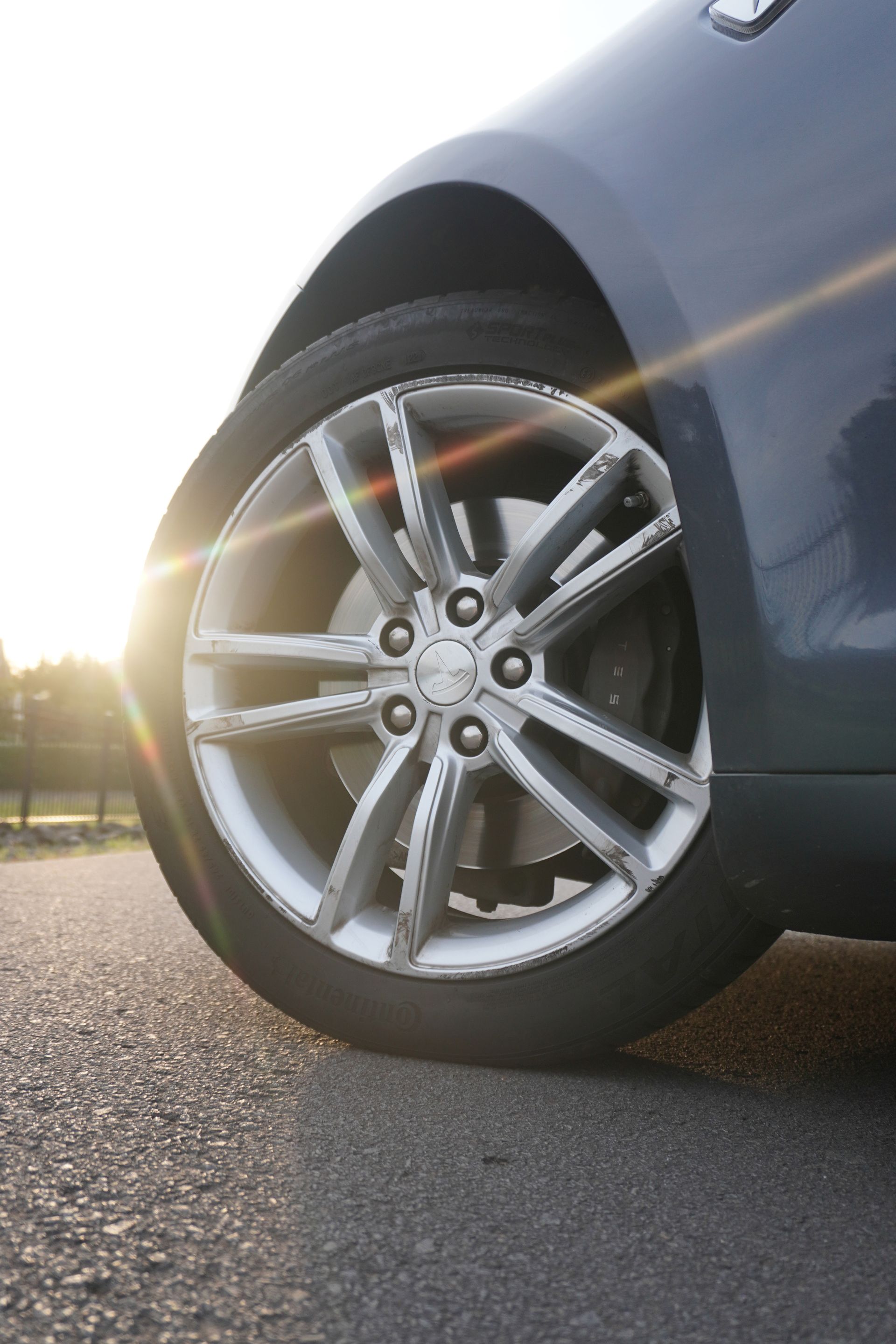 Close-up of a silver car wheel and tire on a sunlit road at sunset