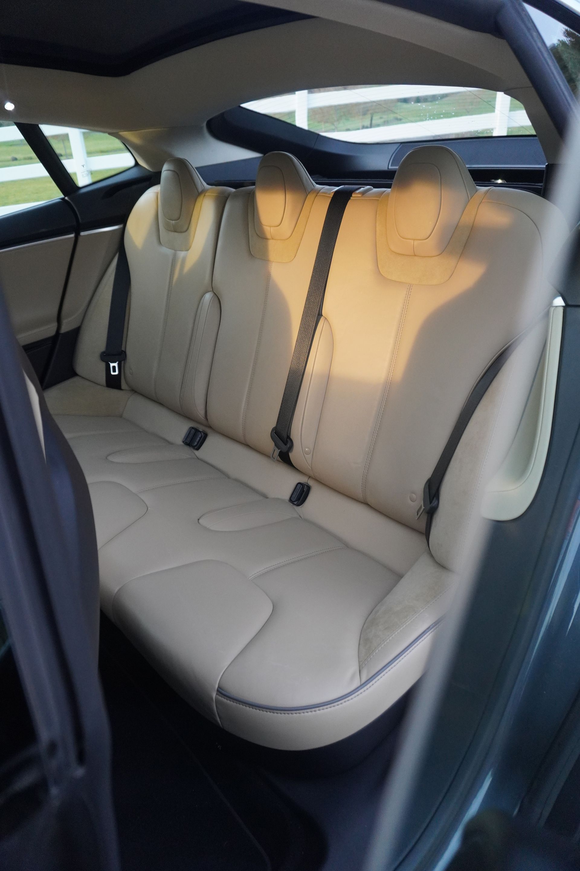 Beige rear car seat with three headrests and seatbelts, viewed from the open door