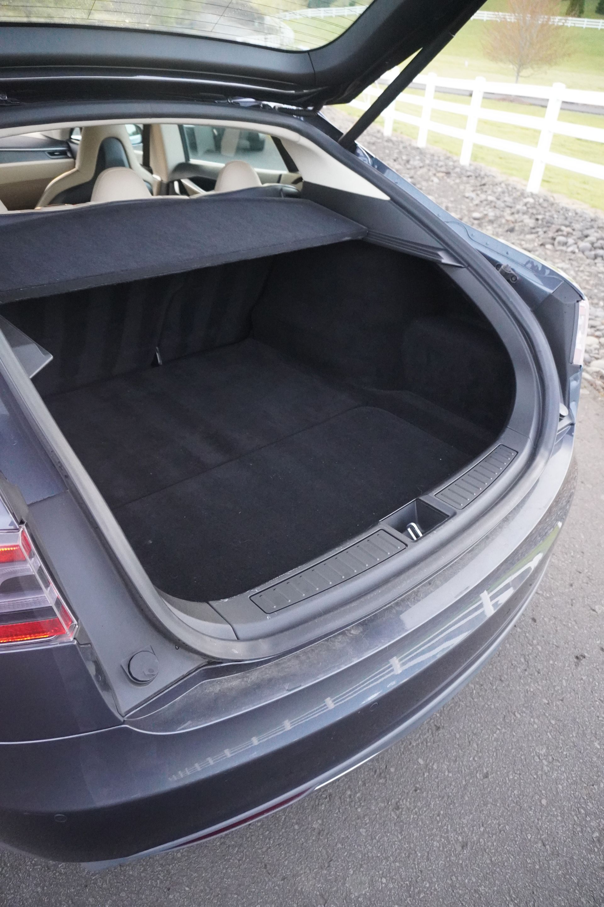 Open car trunk with black cargo liner and rear seats folded down, parked on a wet road.
