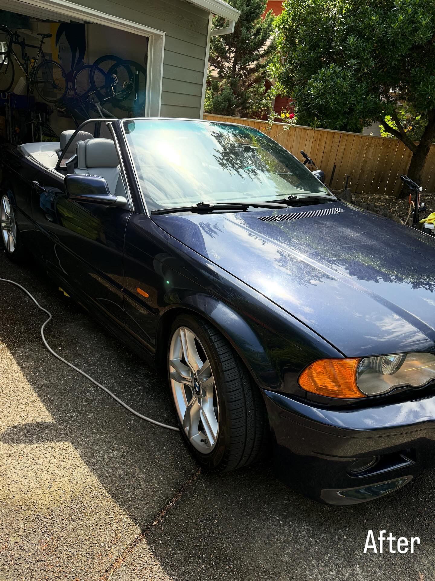 Black convertible parked in a driveway, front three-quarter view in sunlight.