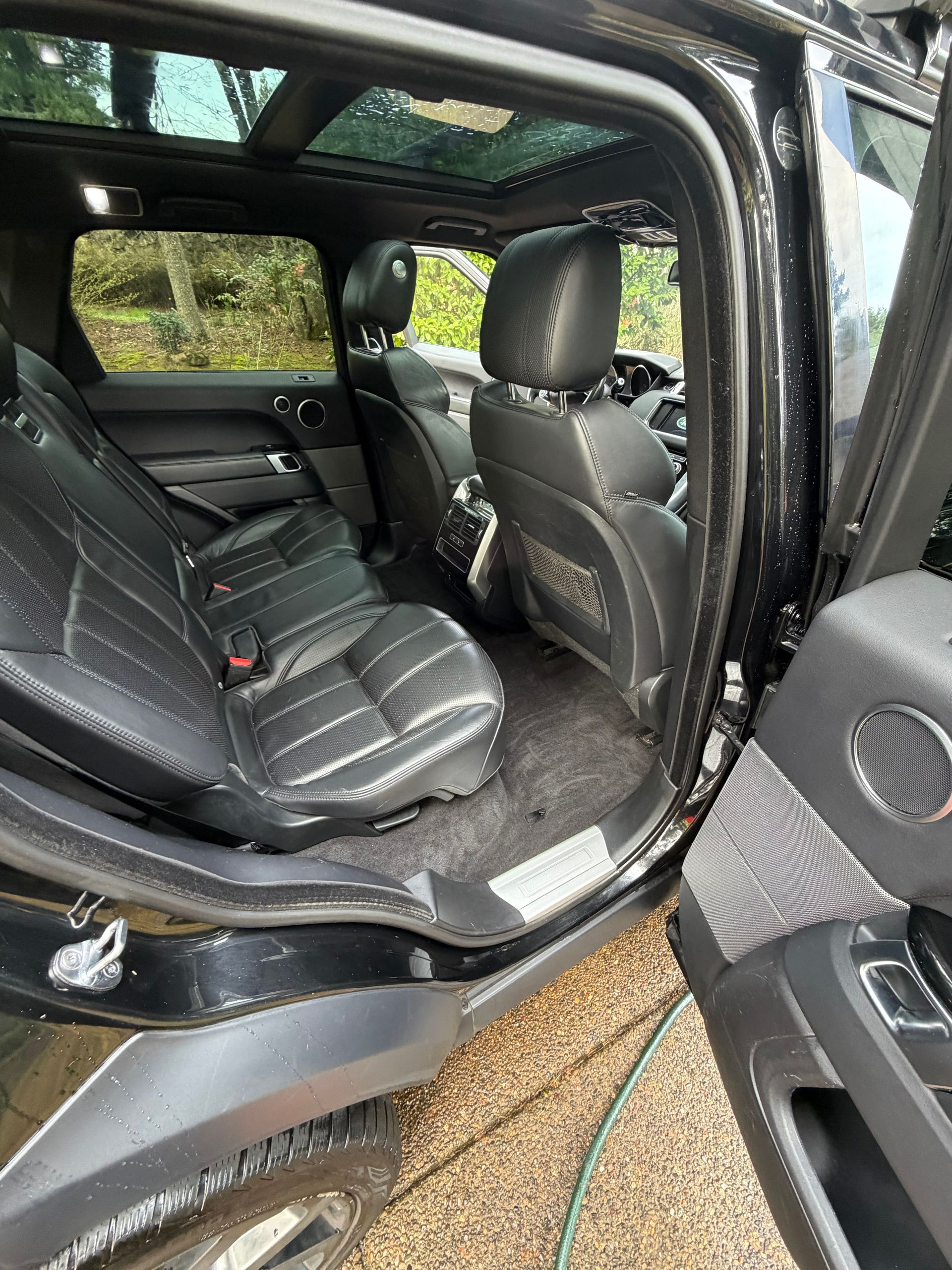 Black car interior with rear passenger door open, showing folded seats and a side step outdoors.