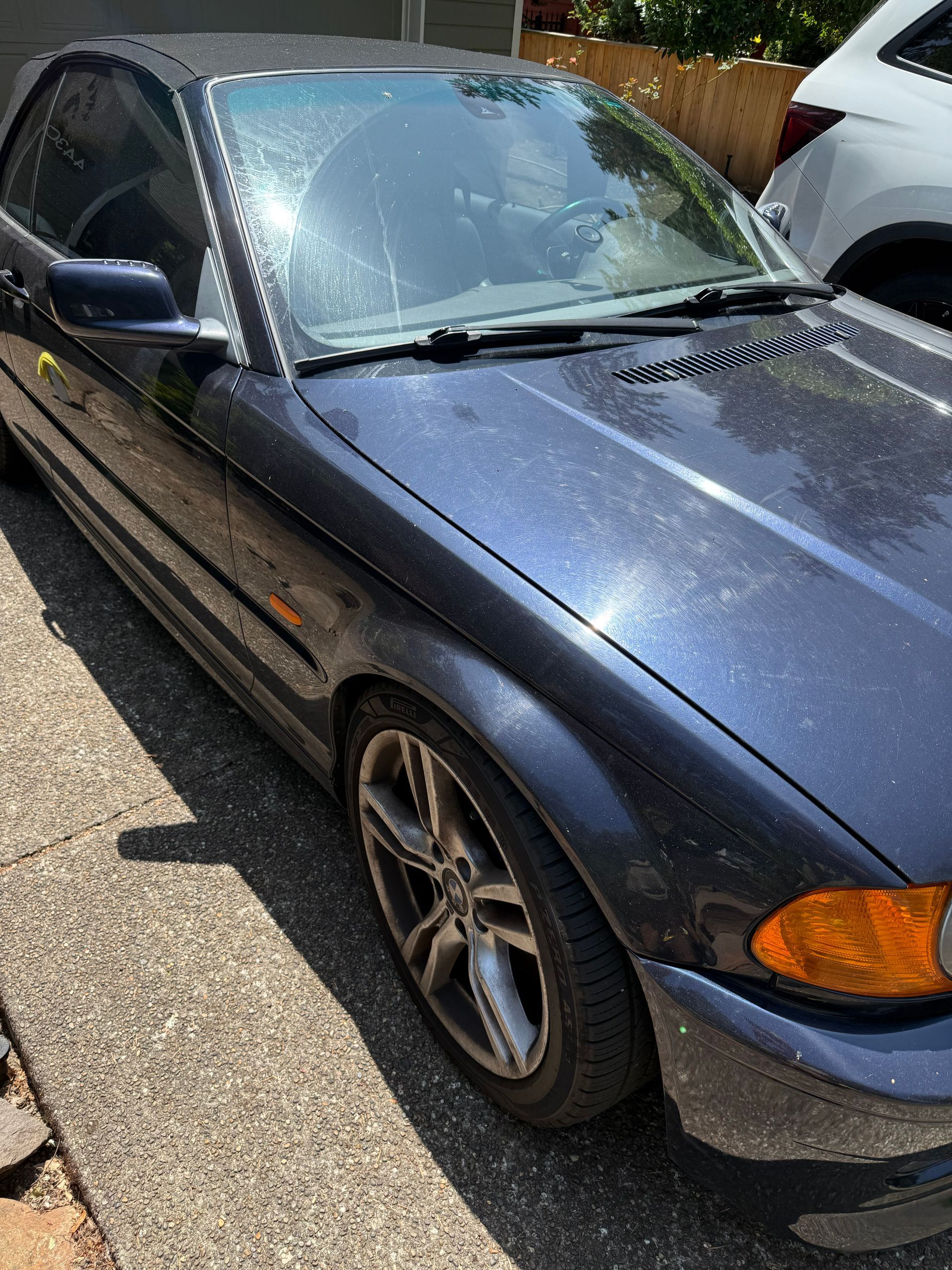 Dark blue sedan parked outdoors in daylight, front-left view, with sunlight on the windshield and hood