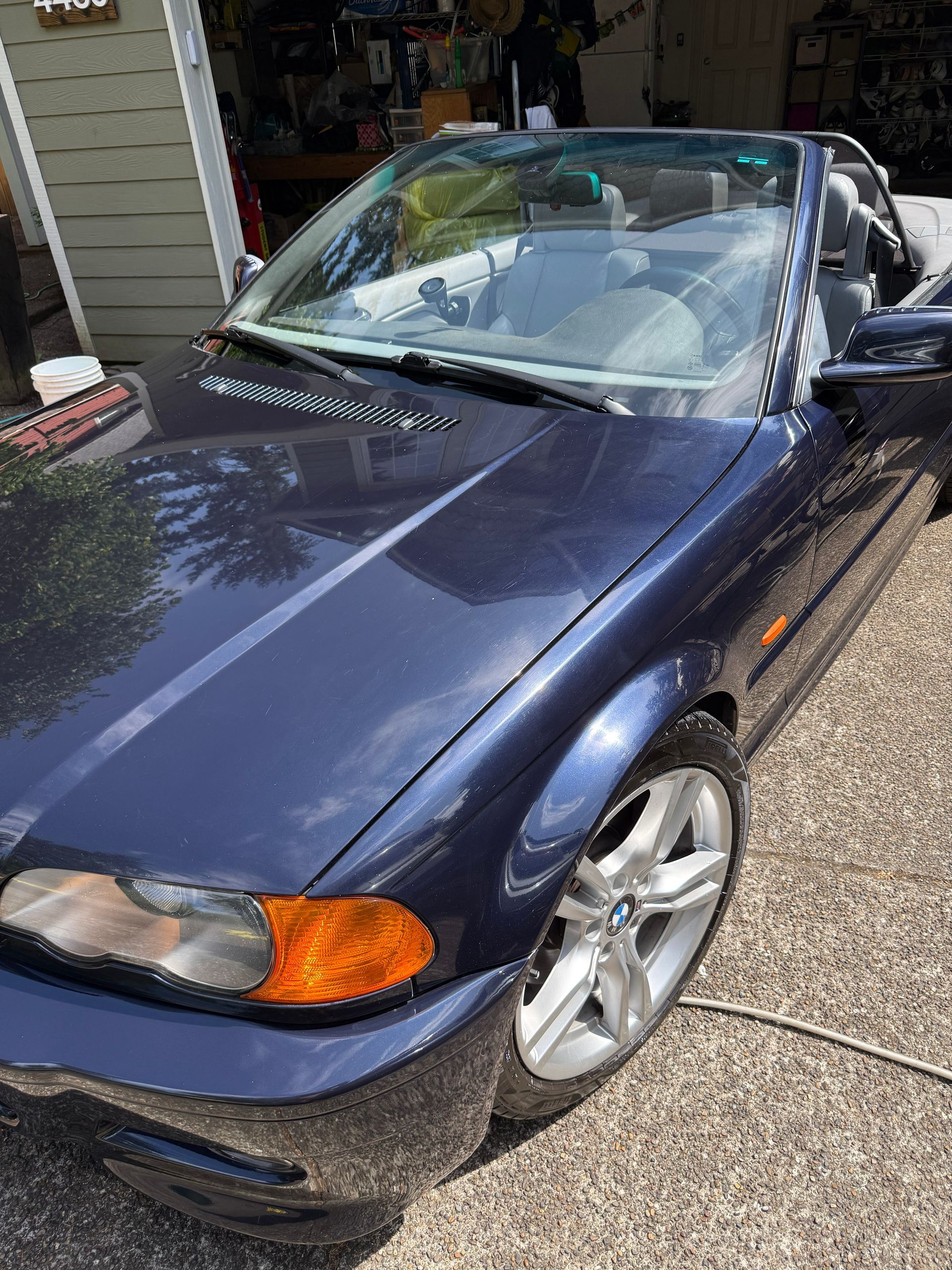 Blue convertible car with a shattered windshield parked in a driveway with debris on the hood
