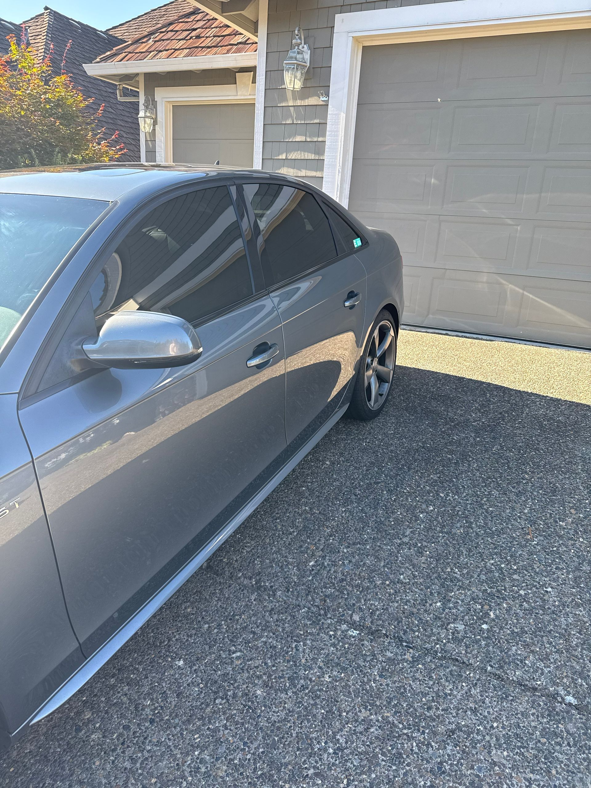 Gray sedan parked in a driveway beside a garage on a sunny day