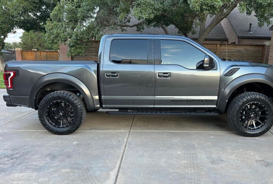 Gray lifted pickup truck parked in a driveway, side view, with black wheels and tinted windows