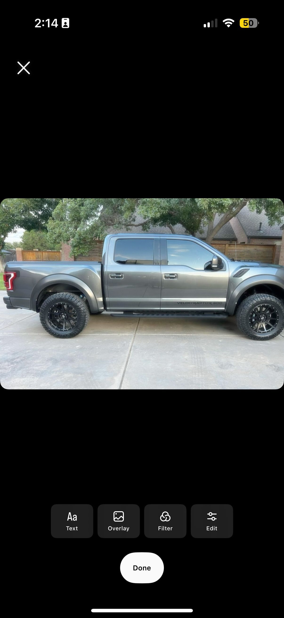 Gray lifted pickup truck parked on a driveway beside trees and greenery
