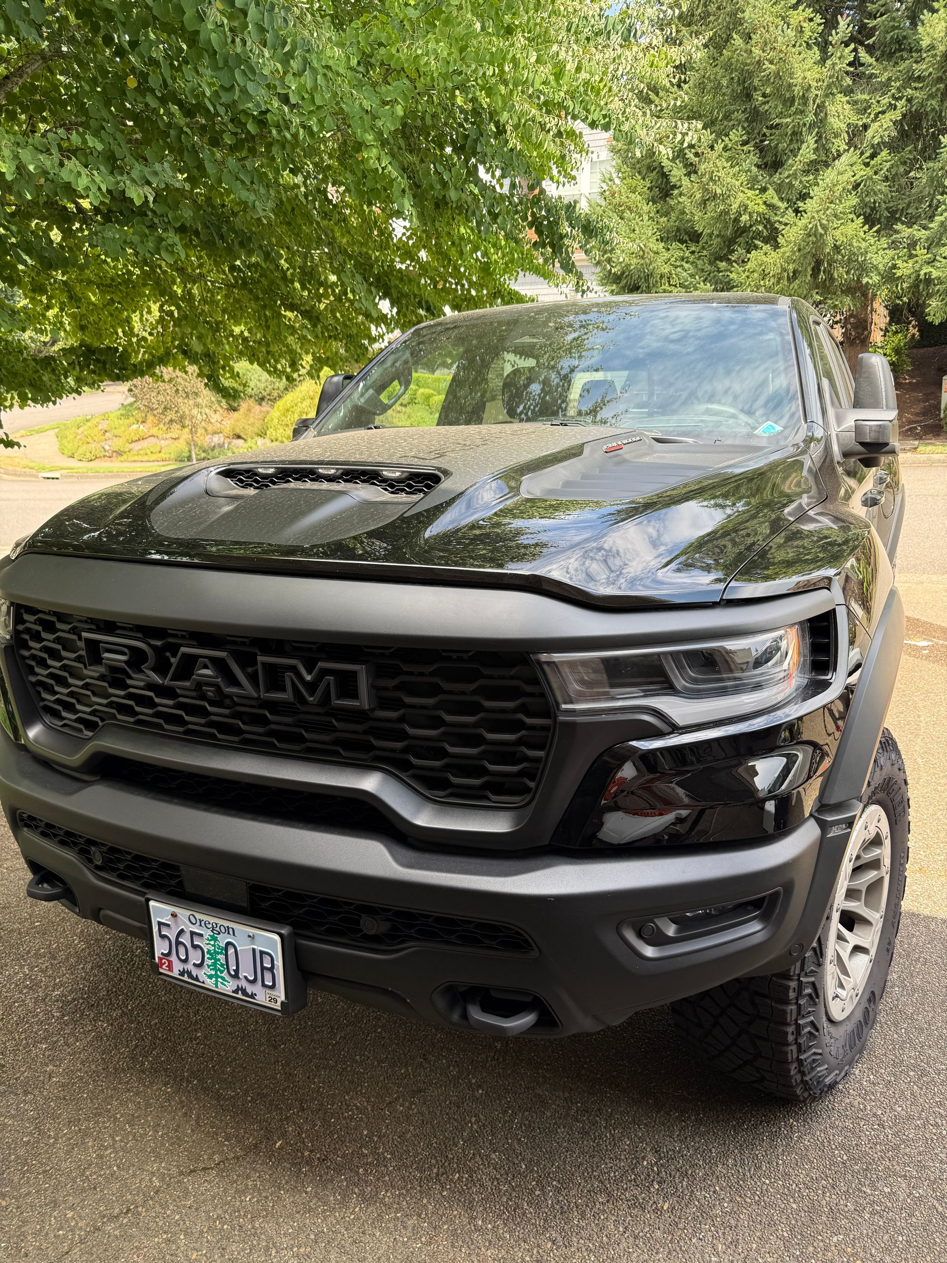 Black RAM pickup truck parked on a tree-lined driveway, front view with tinted windows and off-road tires