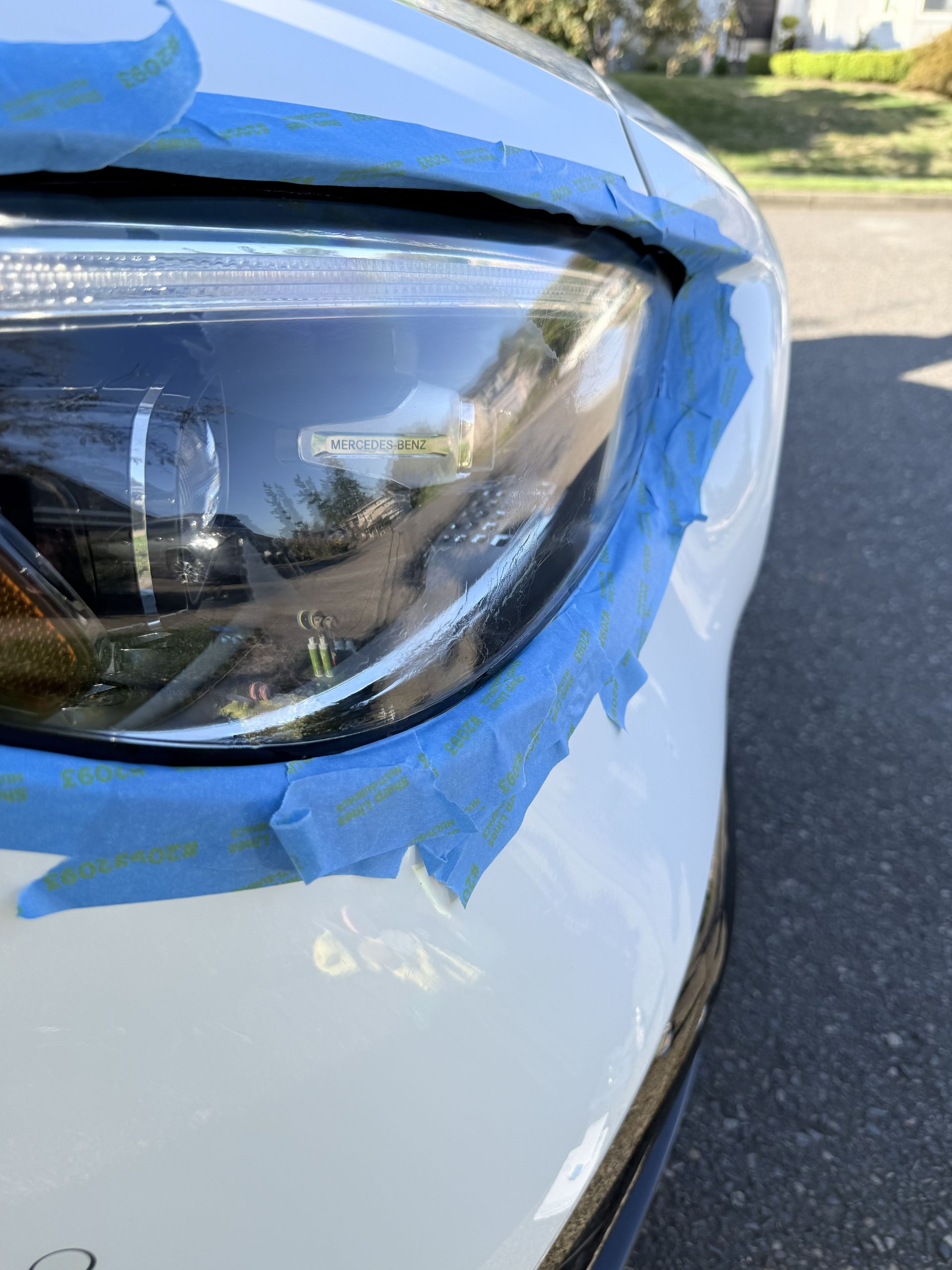 Close-up of a white car’s headlight with blue painter’s tape around the edges